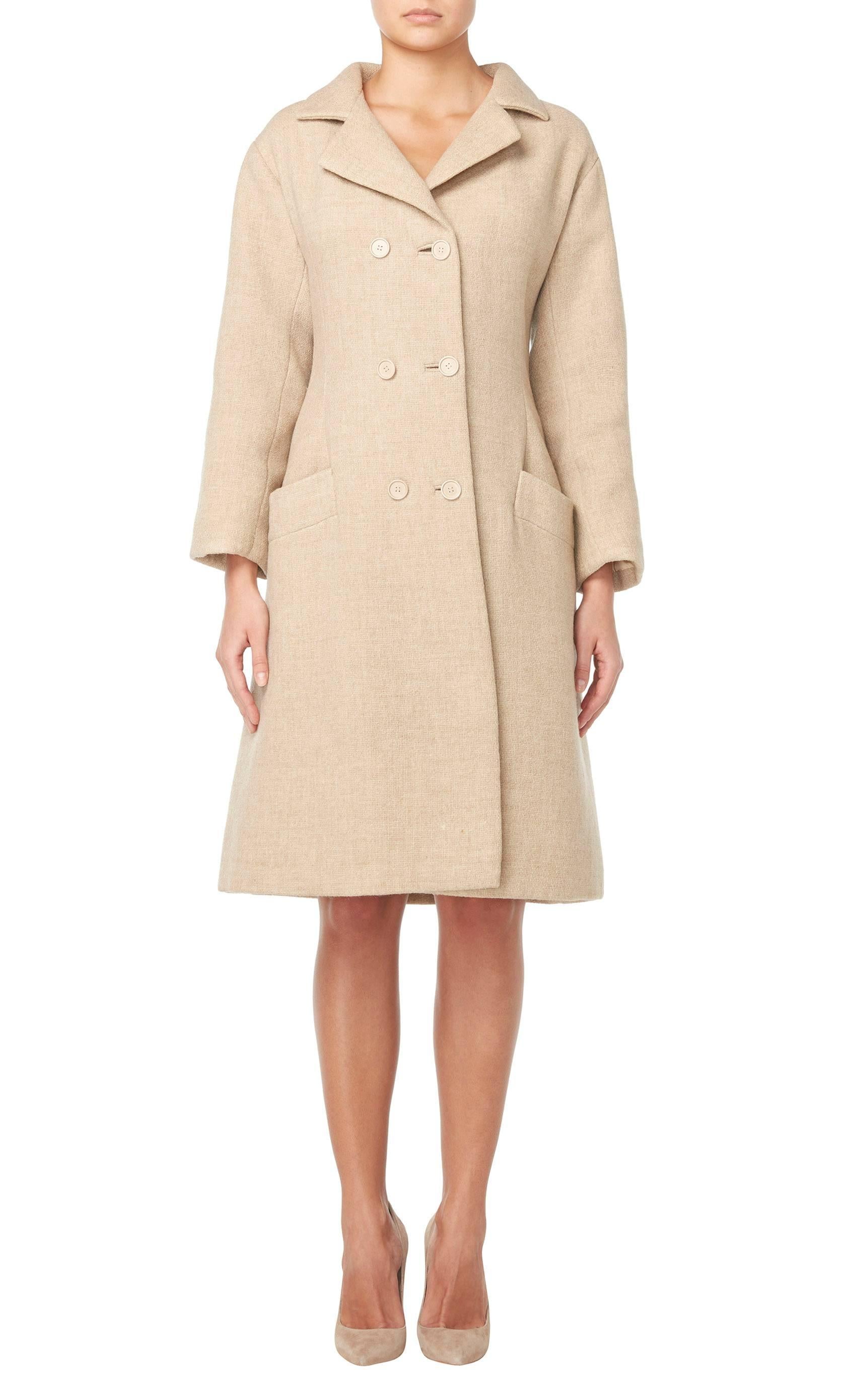 This sharply tailored haute couture coat by Balenciaga for his Eisa label will be sure to become a wardrobe staple. Constructed in a gorgeous shade of oatmeal wool the double-breasted coat features a double lapel collar and a half belt to the rear.