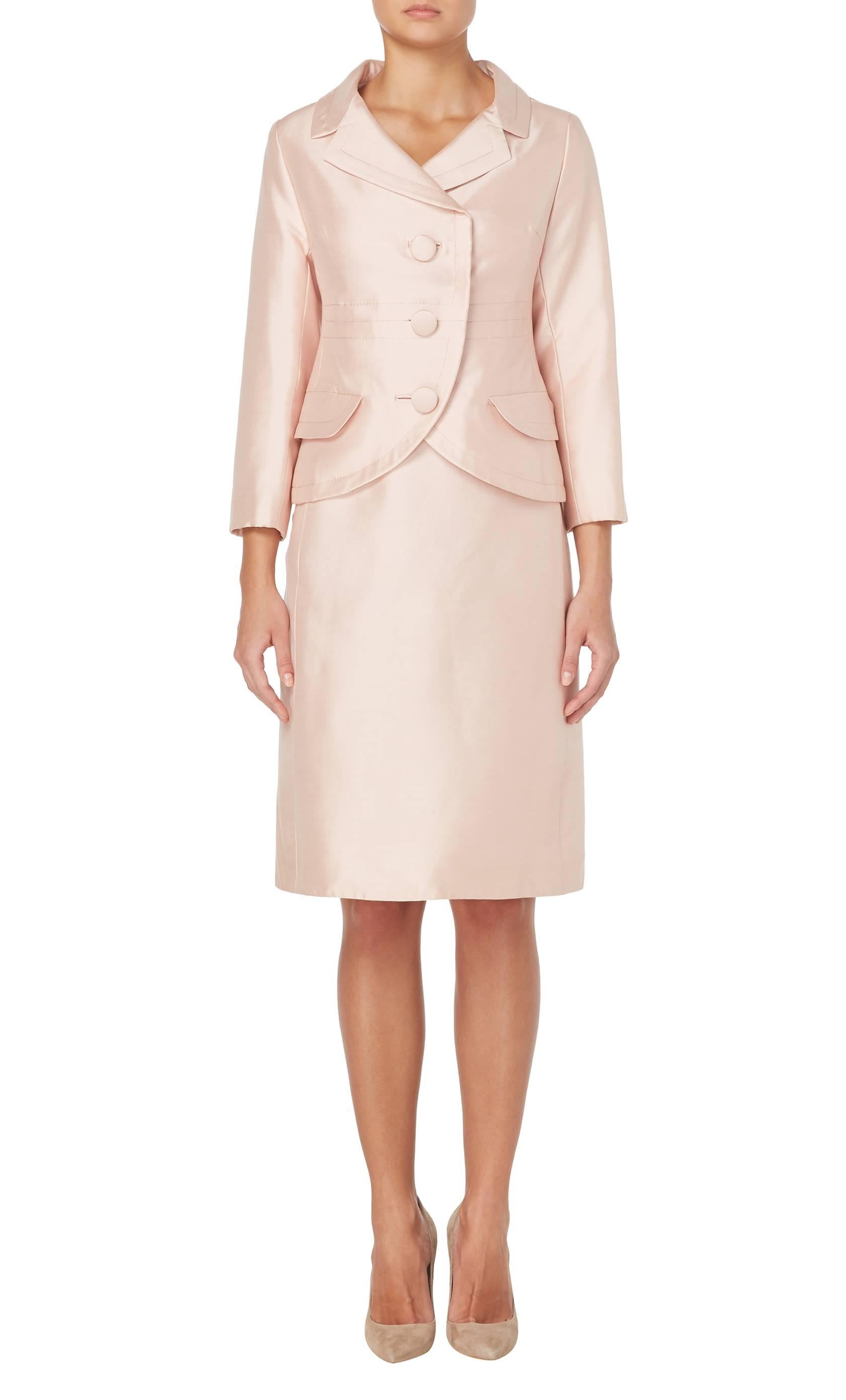 This Christian Dior skirt suit is ideal for weddings and summer events. Constructed in pale pink silk, the jacket features a flattering wide collar, bracelet length sleeves and decorative pocket detail on the hip, while the skirt has a slim fit and