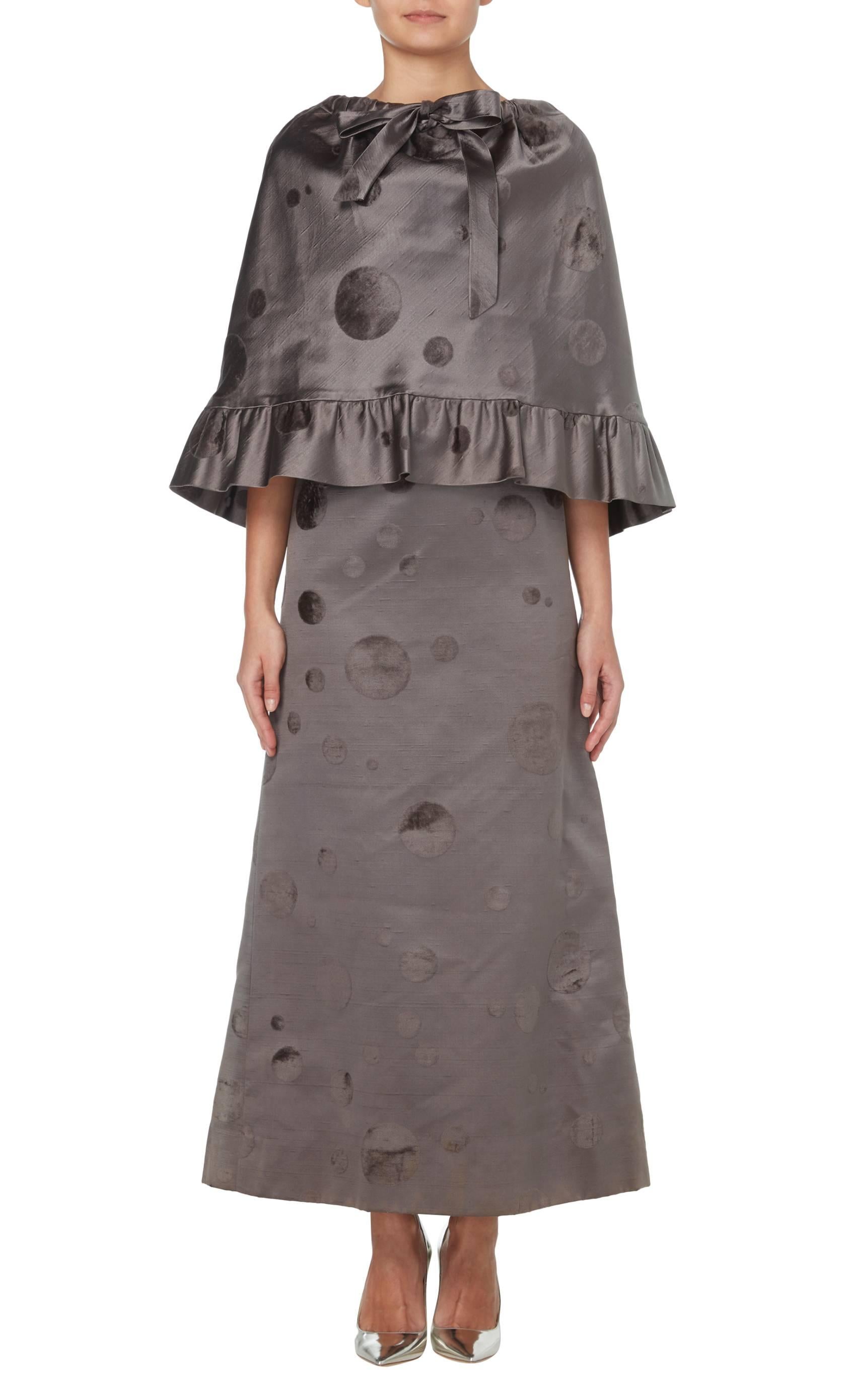 A fantastic statement piece, this Pierre Cardin full-length dress and matching capelet is perfect for black tie events. The pewter silk features flocked-effect polka dots in varying sizes, which give a subtle contrast in texture and colour while