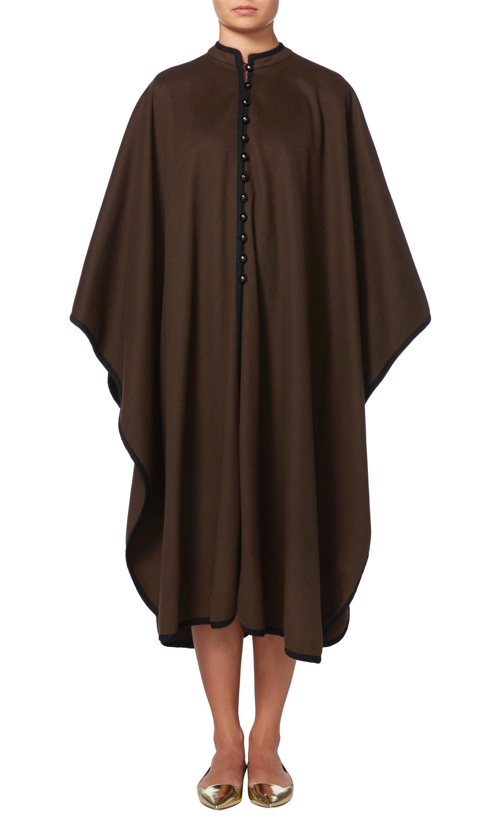 This Yves Saint Laurent cape is a fantastic coverup for cold winter days. Constructed in brown wool and featuring a contrasting black braid, the cape has a standing collar and buttons to the front. Throw on over jeans for weekends in the country or