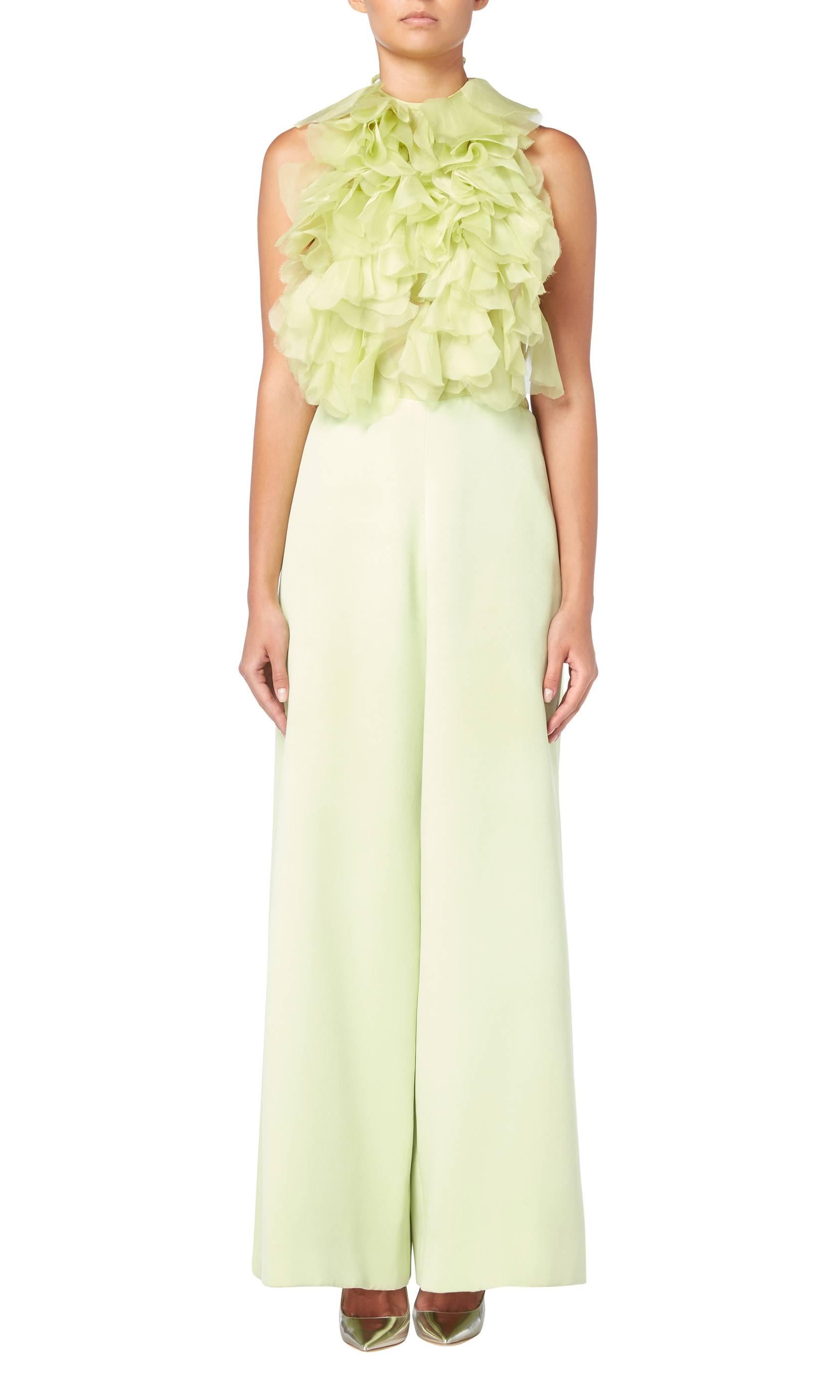 This stunning haute couture jumpsuit by Lancetti will make a fabulous alternative to a dress for evening events. Constructed in citrus green silk, the halter neck jumpsuit is backless and features organza petals to the bust, creating a ruffled bib.