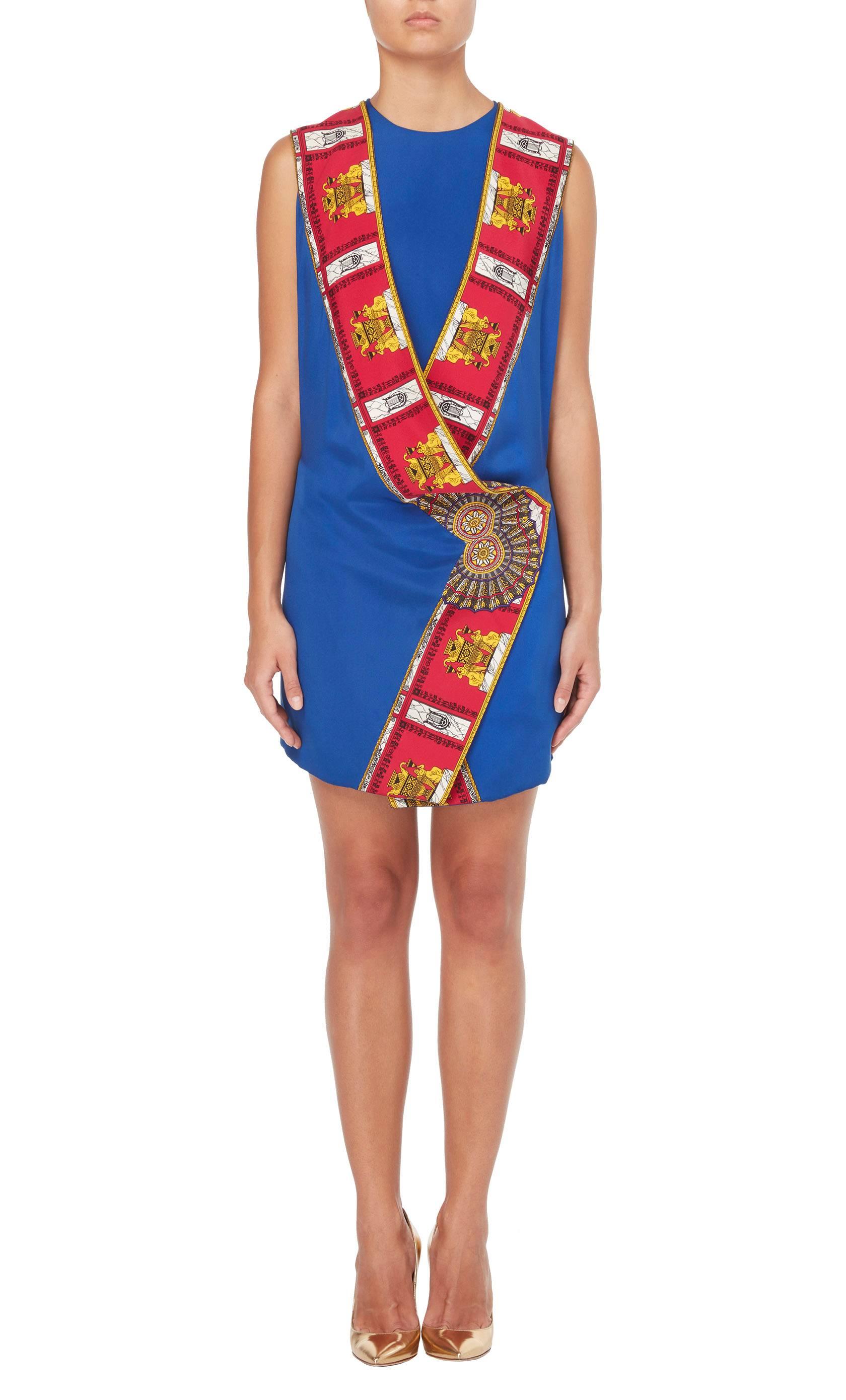 As seen on the Spring/Summer 1991 runway, a variant of this haute couture dress by Gianni Versace was modelled by Naomi Campbell. The dress comprises of a sleeveless blue silk mini dress, with a matching tunic worn over the top. Featuring a wrap