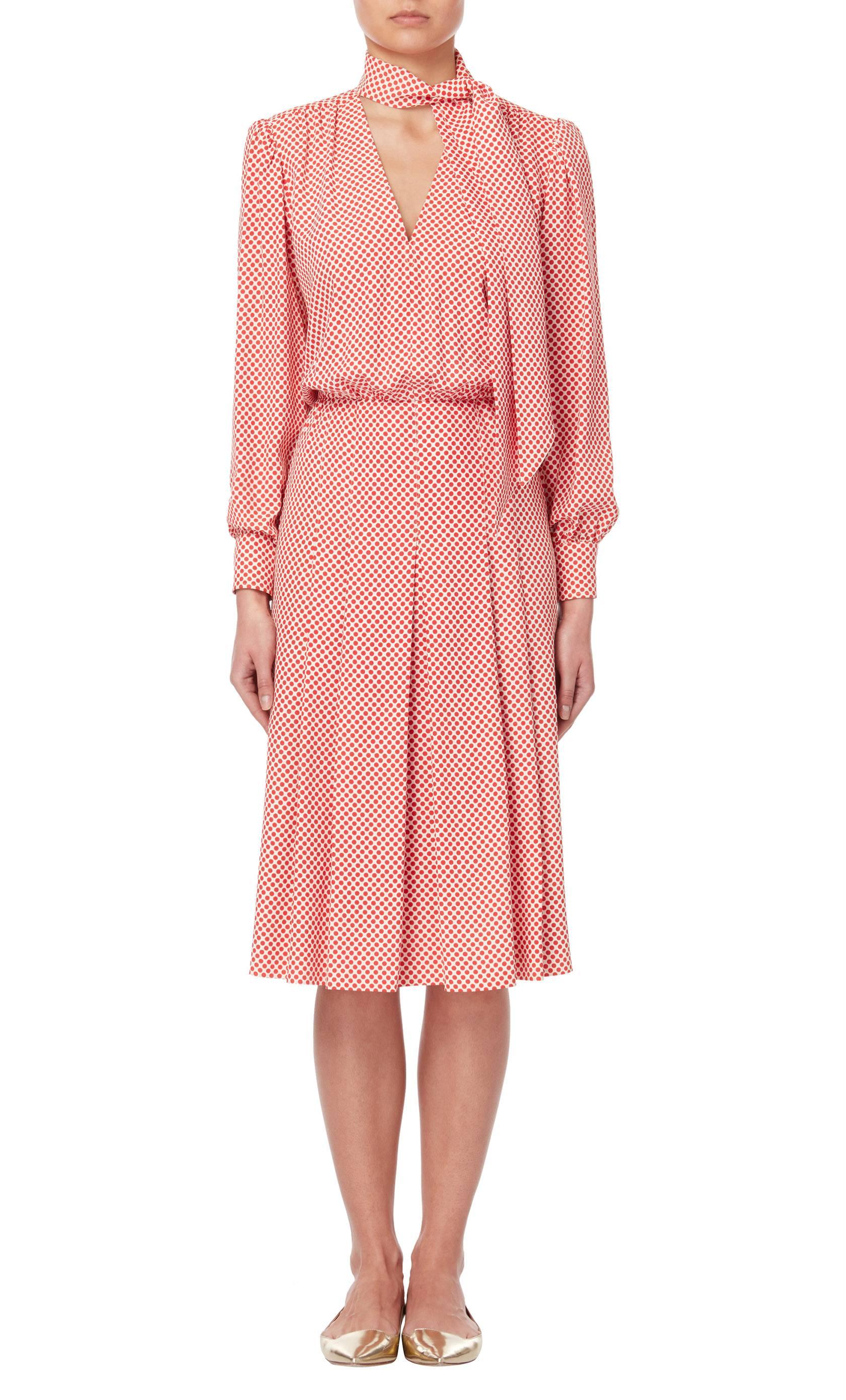 Constructed in ivory and red polka dot print silk, this Yves Saint Laurent dress features a v-neckline and tie detail on the neck. The long sleeves fasten at the cuff with buttons, while the skirt is box pleated to the front.