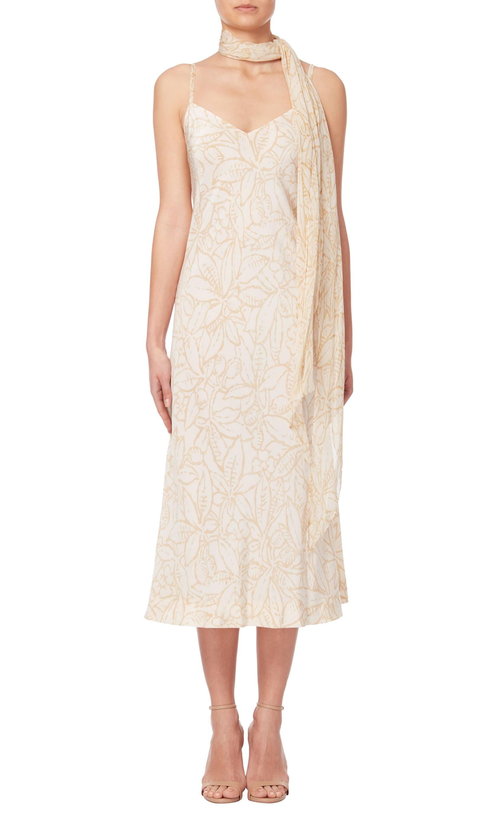 Constructed in ivory chiffon with a beige floral print, this Halston dress has a matching scarf that can be worn at the neck. With delicate straps and a v-neckline, this dress has a minimalist aesthetic. 