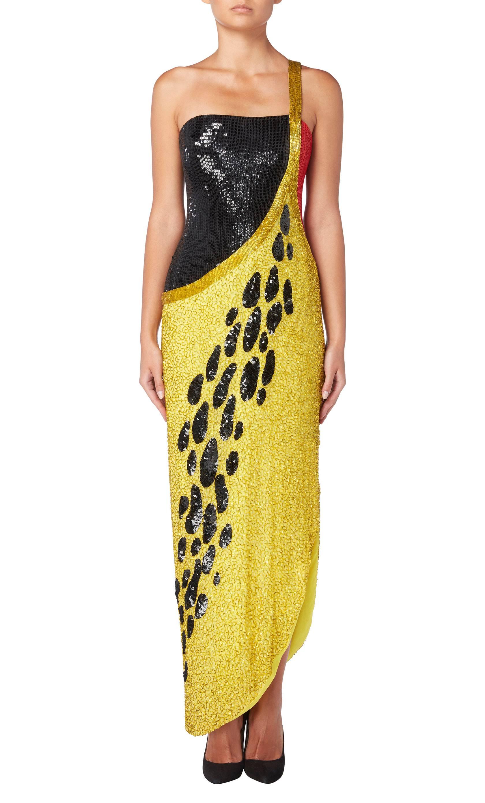 A dazzling option for evening and red carpet events, this Bob Mackie beaded gown is sure to shine. Constructed in yellow silk, the asymmetric gown is embellished with yellow bugle beads and panels of red and black sequins. A black sequin animal