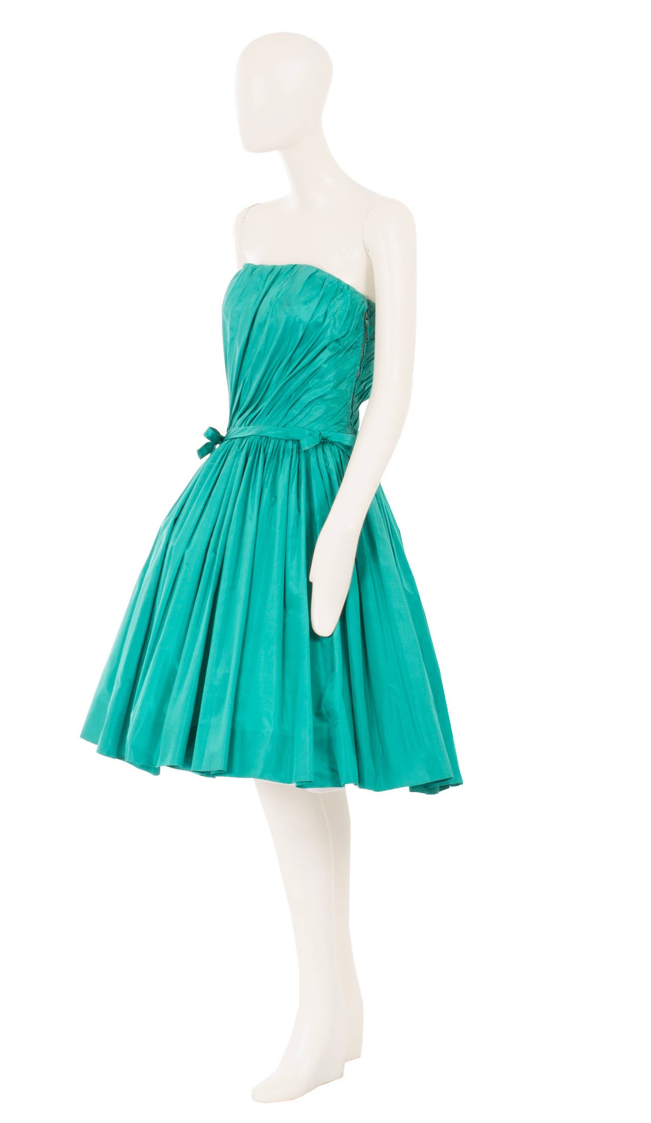 A fantastic party dress in a bold colour, this strapless Jean Dessès cocktail dress is constructed from turquoise silk, pleated diagonally across the bust and gathered around the waist. Boning in the bust offers extra support, while tulle