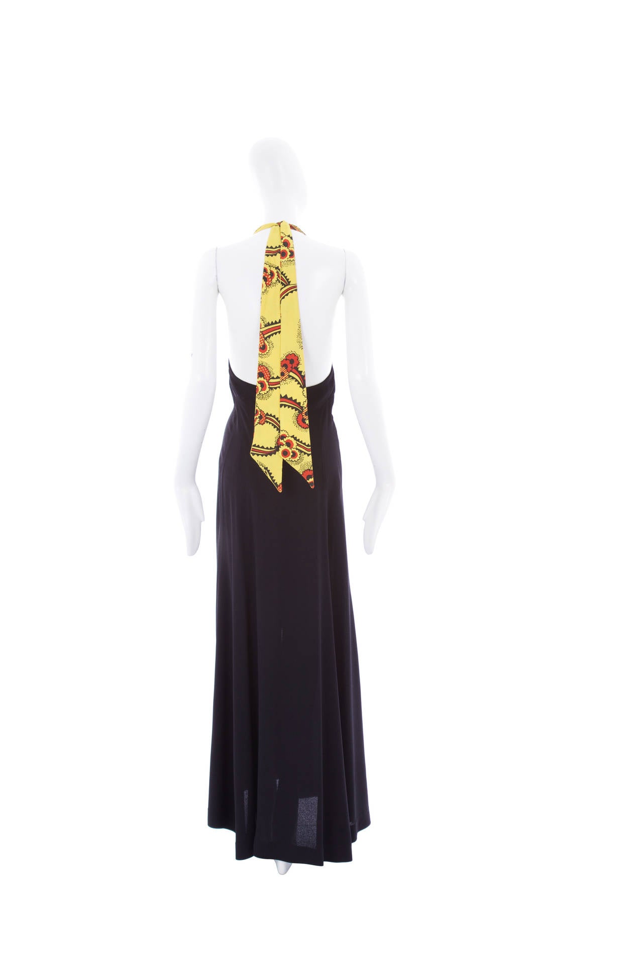 An iconic halter neck dress by Ossie Clark featuring Celia Birtwell’s instantly recognizable Mystic Daisy print on the bust in vibrant shades of yellow and red. The dress ties at the back of the neck and features matching moss crepe buttons. The