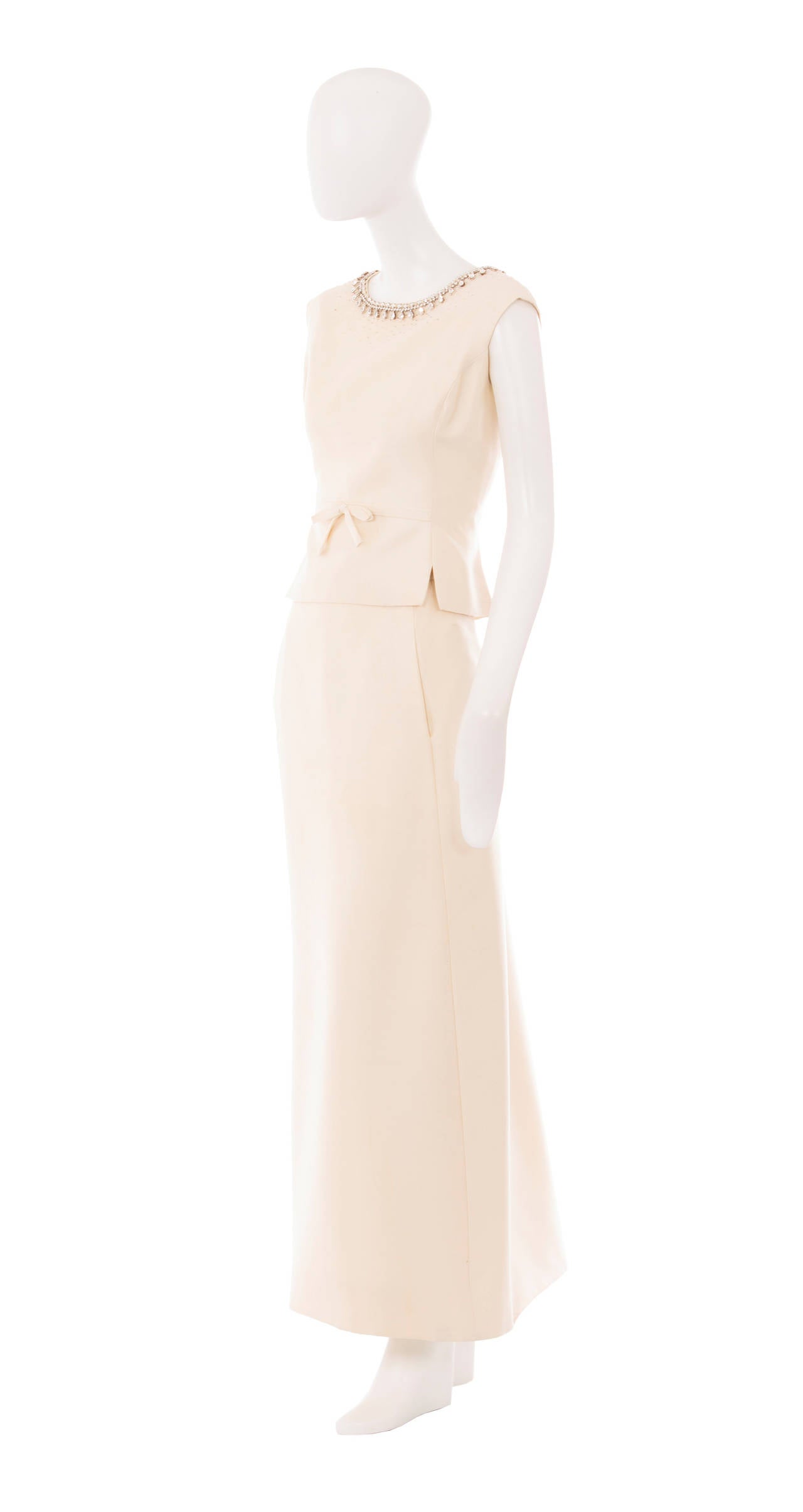 A simply stunning evening ensemble, consisting of a tunic top and column skirt and constructed in ivory silk, this two piece would work wonderfully for a wedding or special occasion. The tunic top features rhinestone detailing on the neckline, with