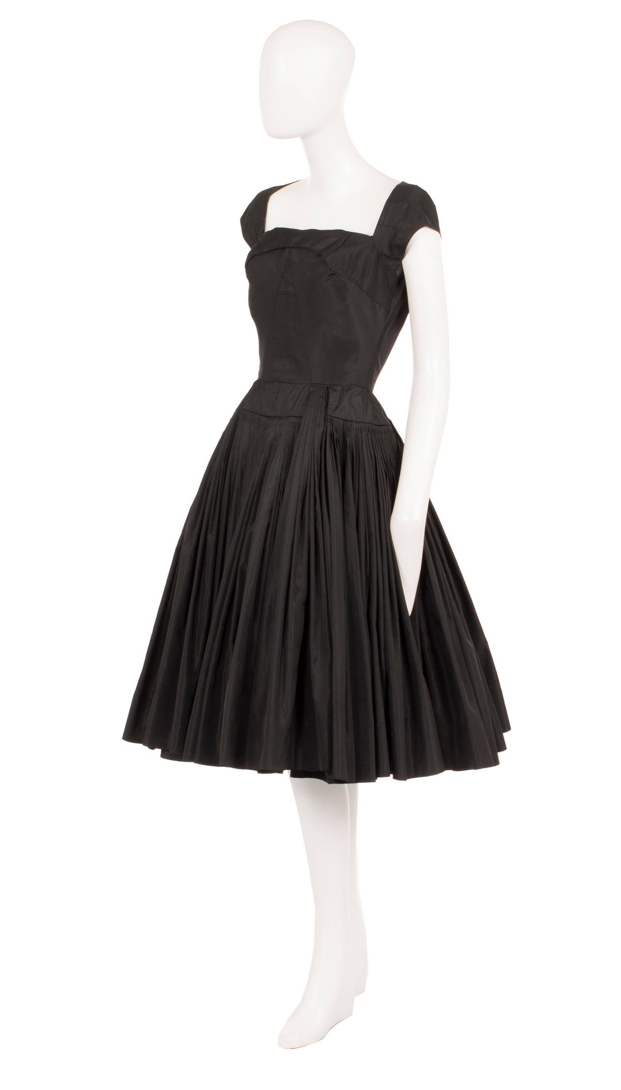 A classic LBD that will work for a multitude of events, this dress is constructed from silk taffeta and features capped sleeves and a square neckline. The wide pleated skirt accentuates the waist and creates a flattering 1950s silhouette. Just add a