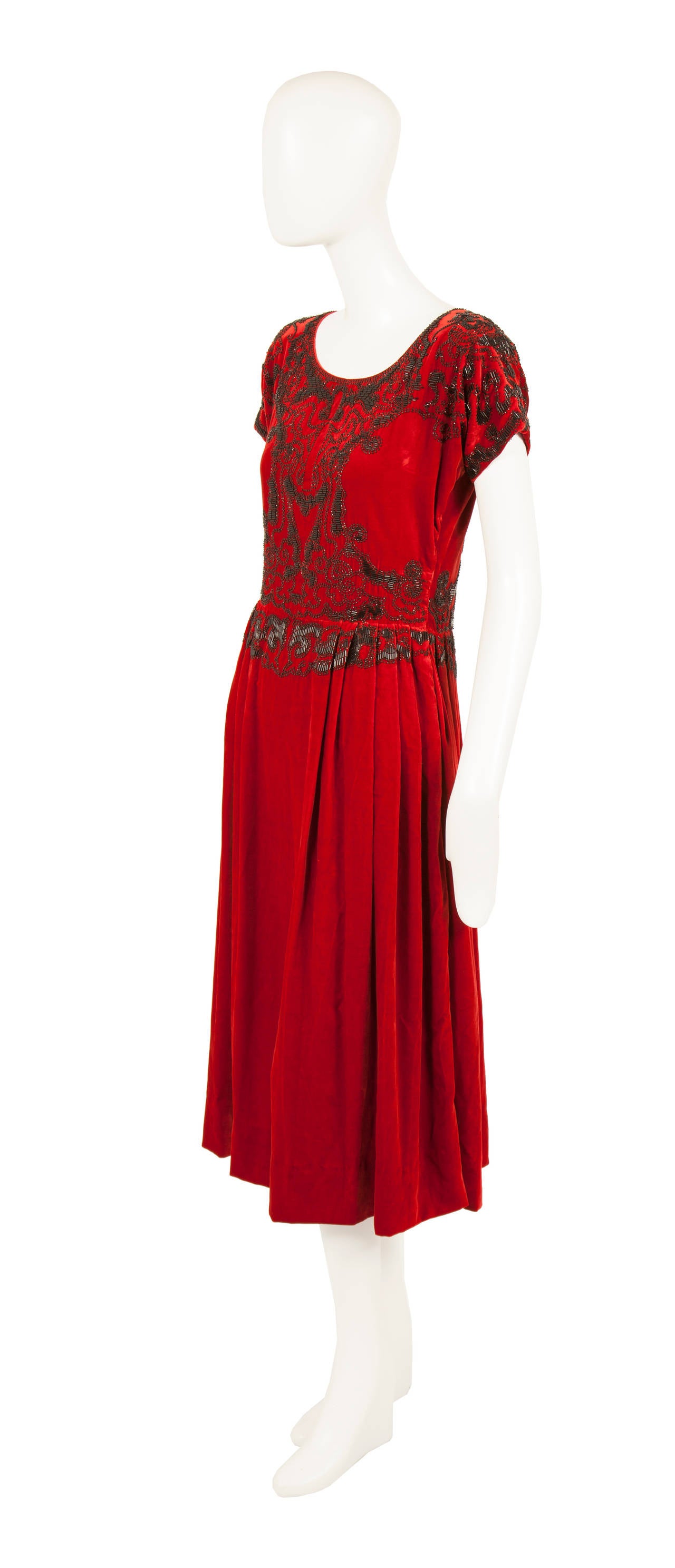 This rare Paul Poiret haute couture cocktail dress is an exceptional example of the designers work. Constructed of the finest ruby red silk velvet, the dress is intricately embroidered with black glass bugle beads on the body and capped sleeves,