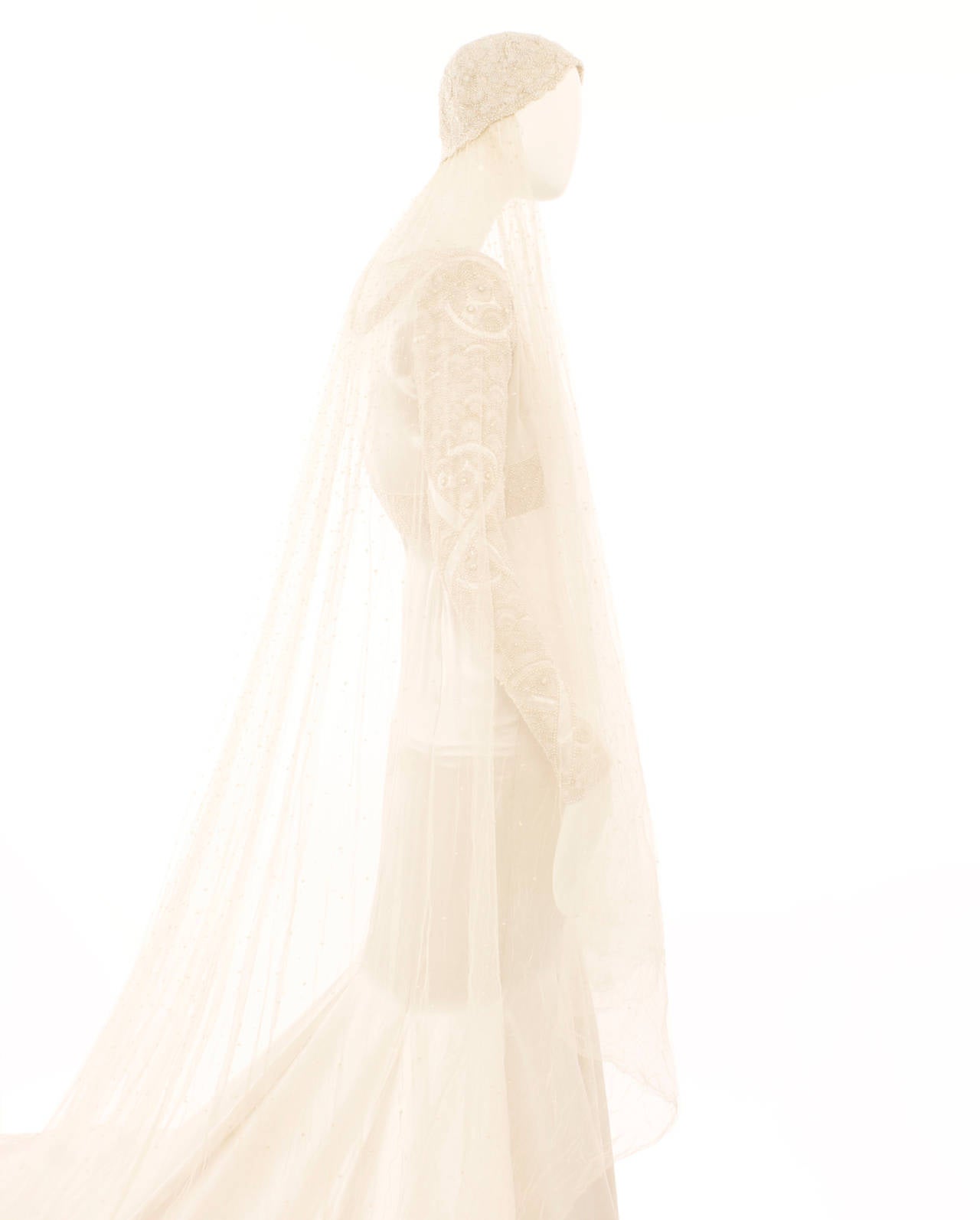 An exquisite piece of haute couture, this bridal gown was designed by the royal couturier Sir Norman Hartnell in the spring of 1931. The gown is composed of bias-cut ivory silk satin, complex seed pearl embroidery and has a sweeping train over eight