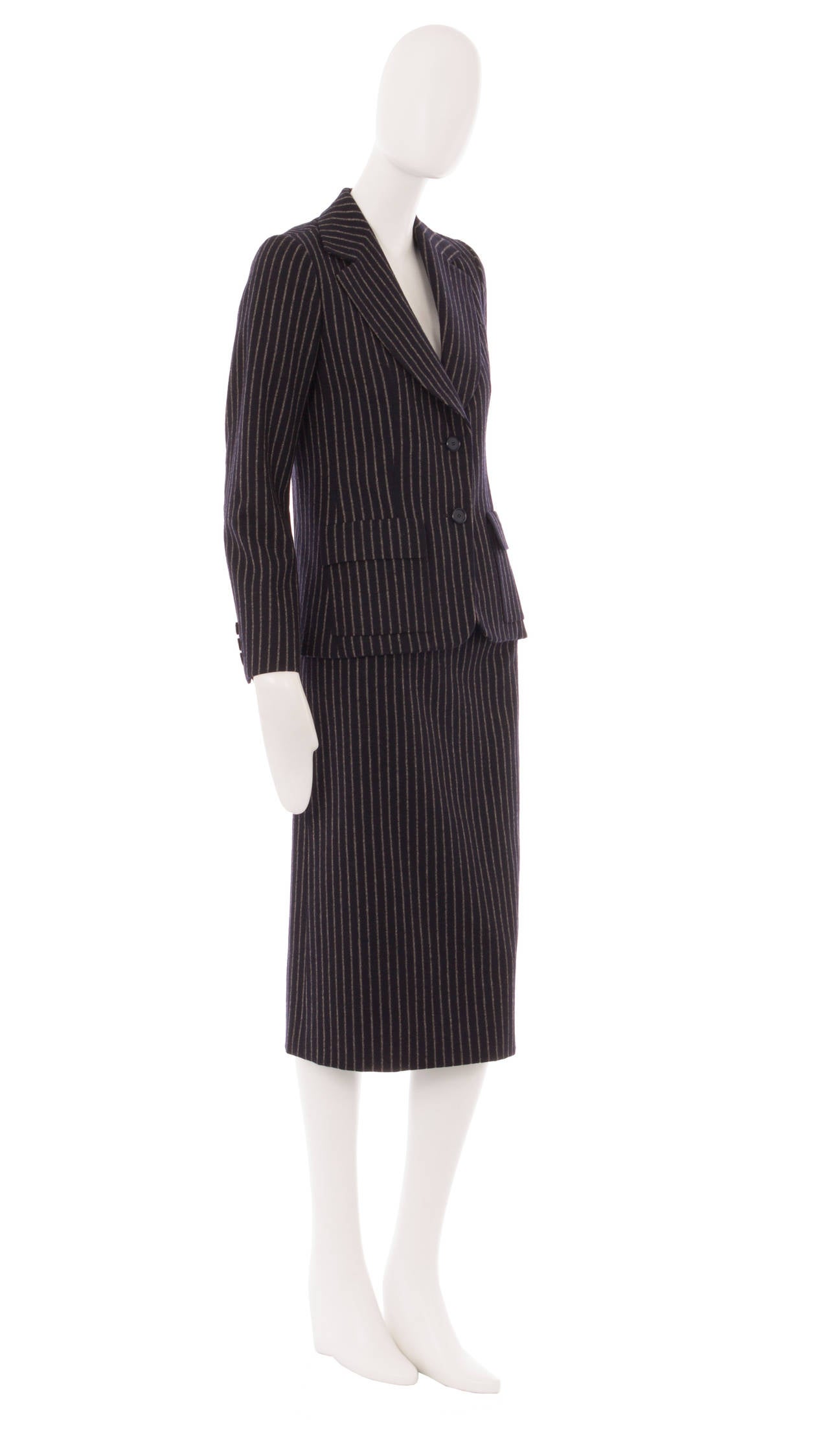 The perfect choice for the office, this Dior skirt suit, constructed from navy wool with an ivory pinstripe, is beautifully cut. The jacket features a double collar, buttons on the waist and outside pockets on the hips, while the skirt fastens with