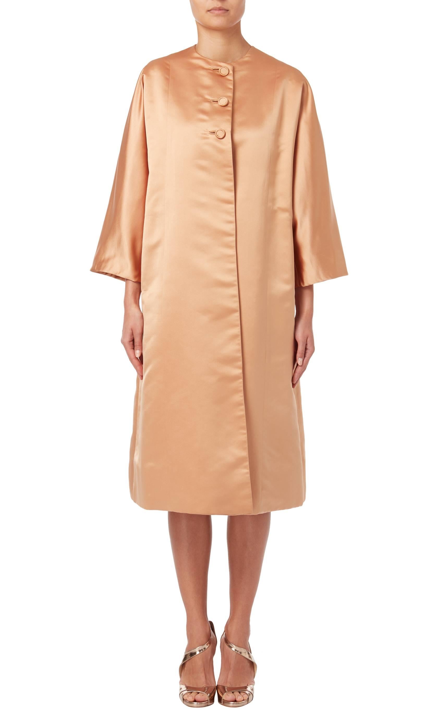 Peach silk coat by George Carmel, circa 1962. The coat features a round neck and is secured by three silk covered buttons to the front.
