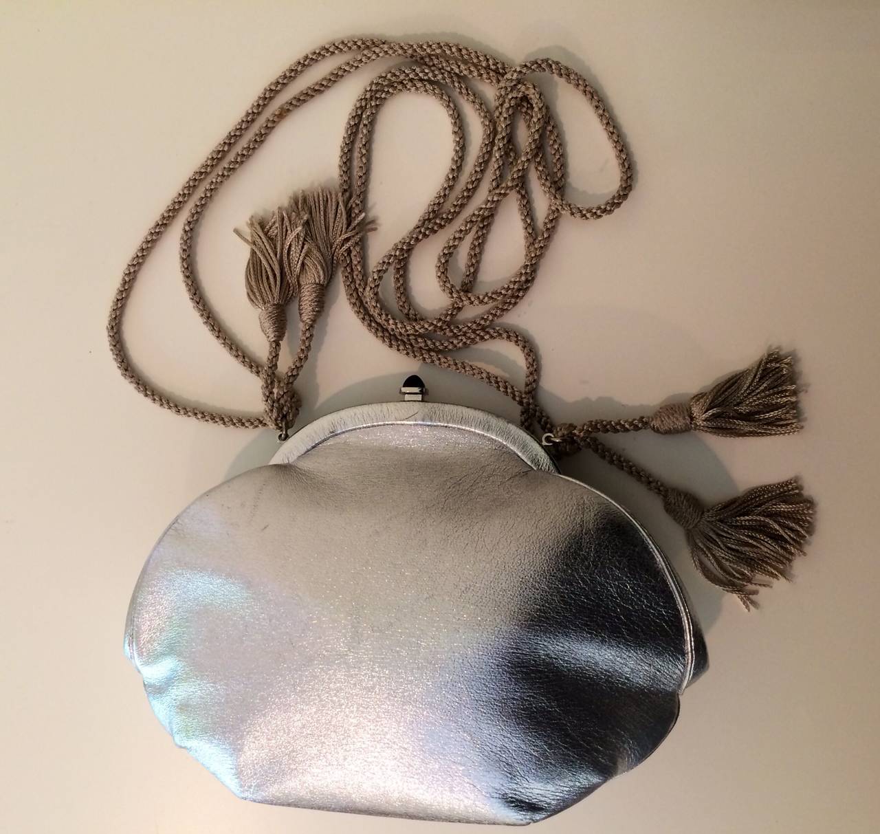 A vintage Judith Leiber silver metallic leather evening bag. Black onyx stone clasp. Silk cord strap with tassels. Strap can be tucked inside and used as a clutch. Comes with mirror and coin purse. Lined in satin.
Excellent