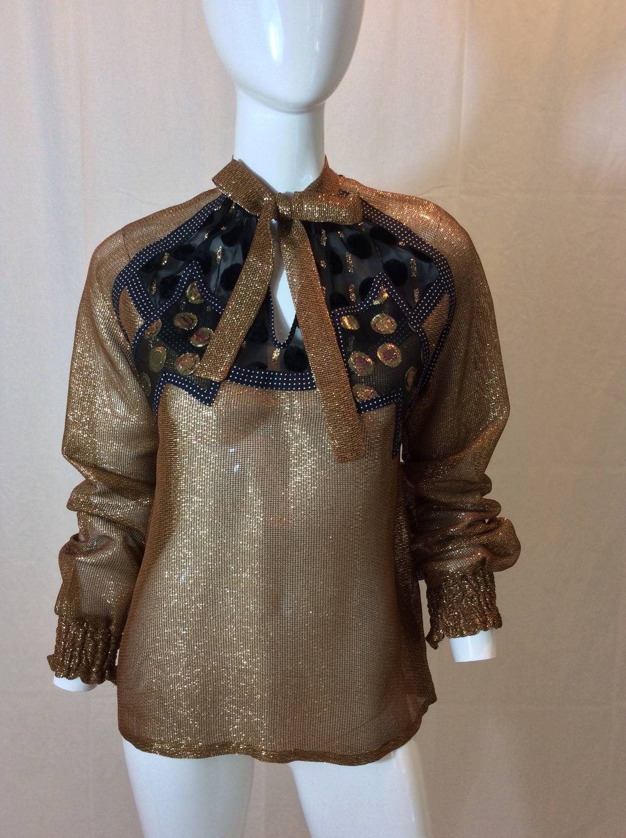 This gorgeous metallic gold and bronze blouse slips over the head with a key hole opening in the front. The fabric content  is unknown and soft to the touch. A black and white polka dot fabric runs along  the raglan sleeve seams and down the sides