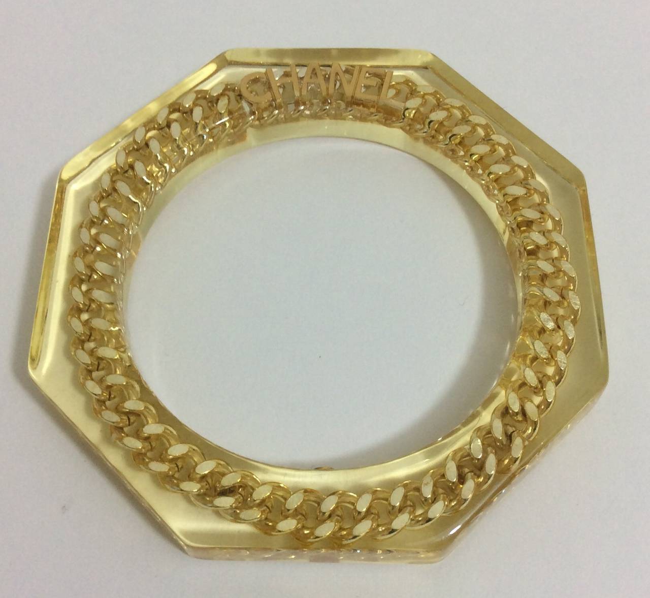 Chanel lucite bangle with a gold a  tone chain set inside the lucite.
Circumference: 7.75