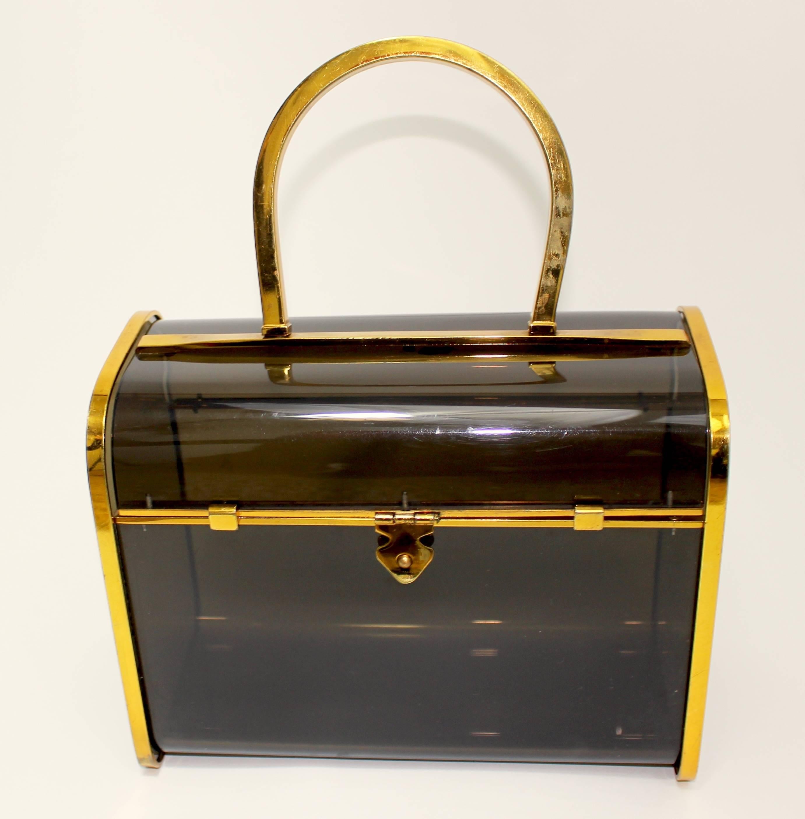 A vintage Judith Leiber translucent smoke color lucite box bag with gold plated frame and top handle.

Very good condition, some plating loss to the gold finish on the handle.

Measurements:
Width. 8 inches
Depth: 4 inches
Height: 6 and 1/4