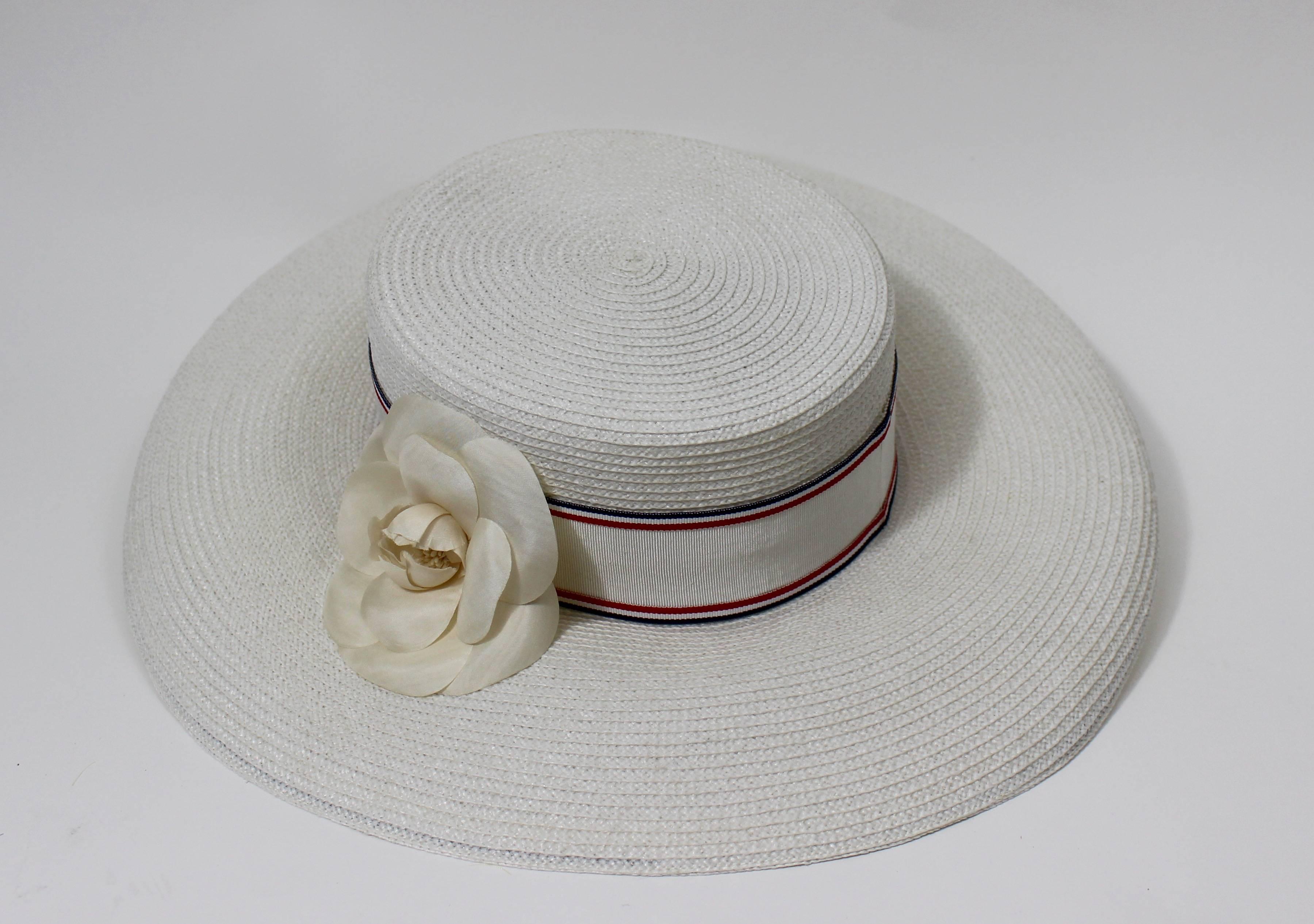 A vintage Chanel white woven hat. 
Grosgrain ribbon band with red and blue stripes.
Camellia Flower.

Excellent condition.
Size: 57

Measurements:
Inner circumference: 21.5 inches
Crown: 3 and 1/4 inches tall
Brim: 4.5 inches