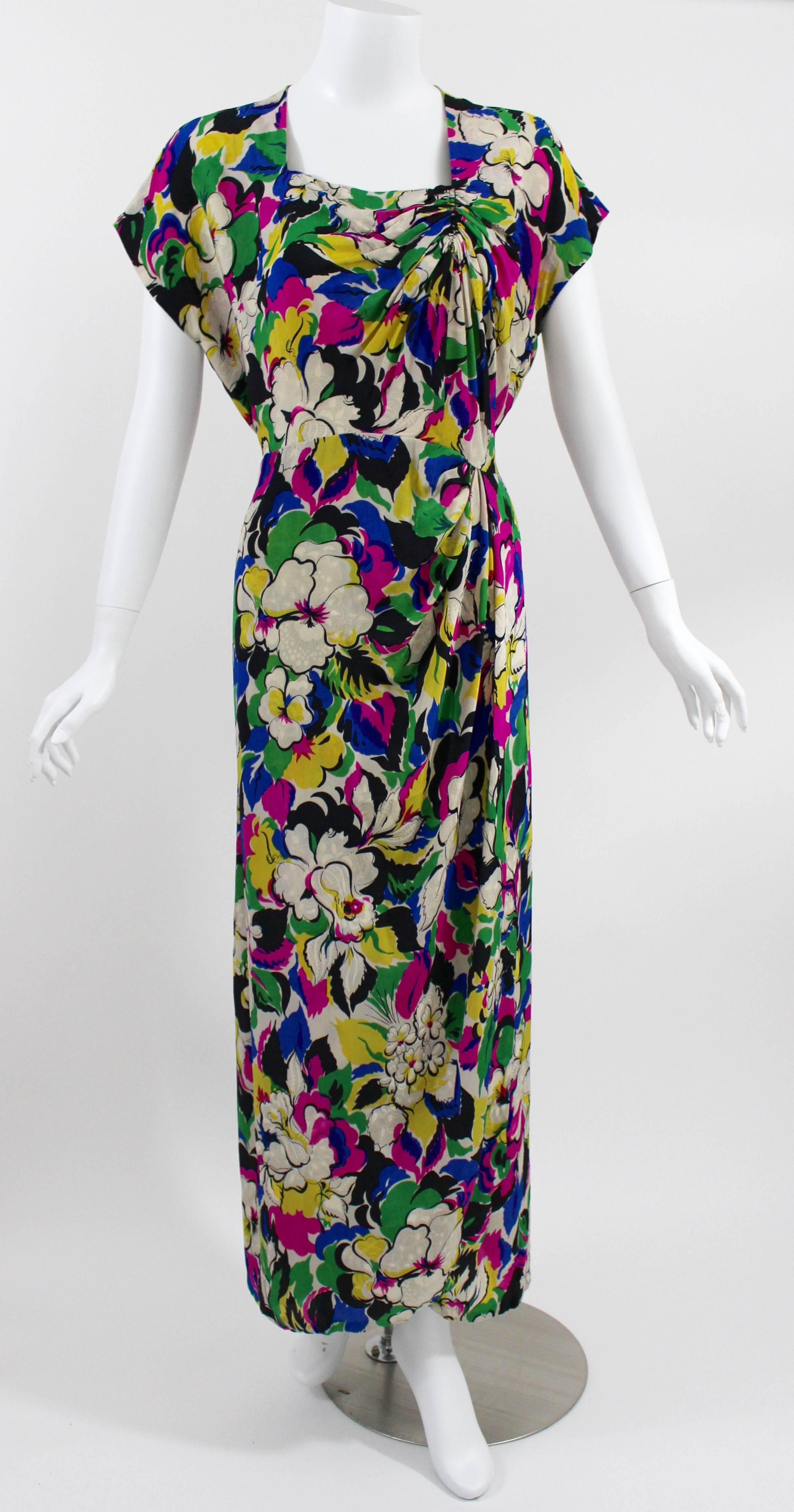 A beautiful 1940s colorful floral garden dress. The dress is fashioned in a light and drapey silk damask with a bright floral print in blue, fuchsia, green, yellow, ivory and black. With short sleeves , a square cut neckline and a hint of ruched