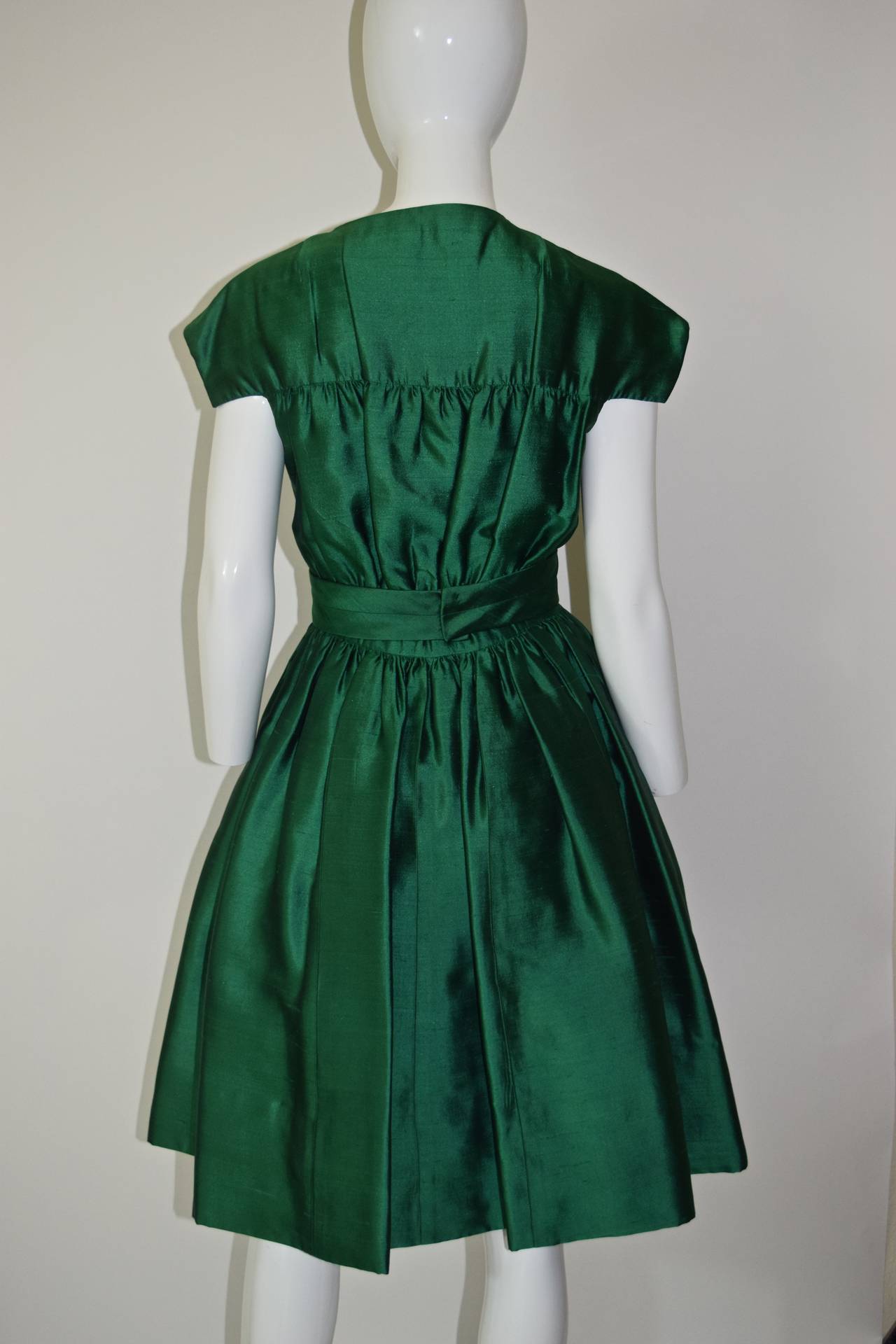 This is an exquisite 1950's dress from Henri Bendel.   Made from  a beautiful  raw silk in the most  brilliant emerald green color that I have ever seen in a fabric.
Three large dark green plastic buttons down the front of the dress and a hidden