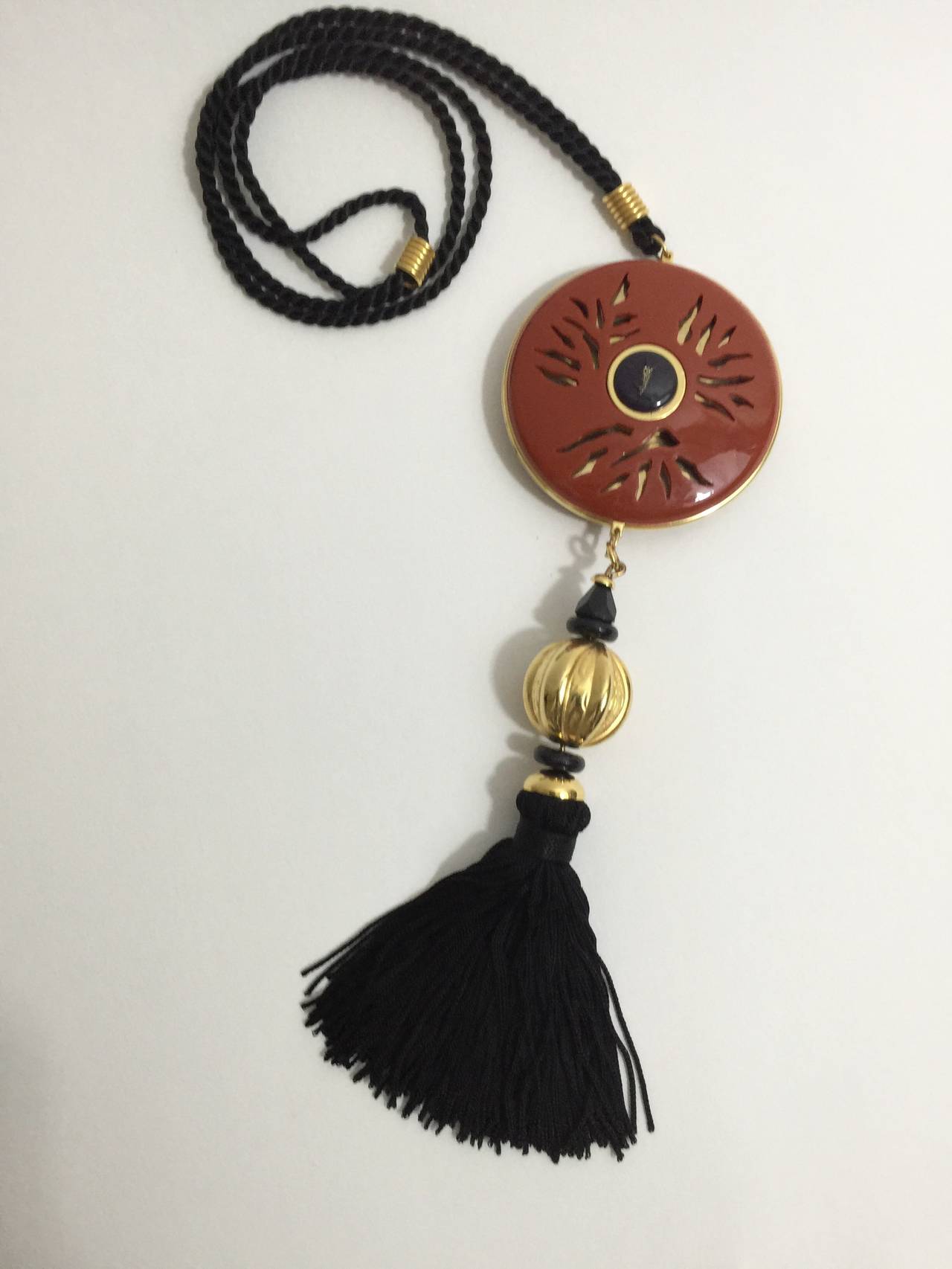 This Vintage YSL Opium Tassel Necklace is beautiful and collectable.  
Opium perfume was first released in 1977,and  the opium necklaces have been discontinued since the mid 1980's. 
A deep orange disc pendant with open work detailing and YSL