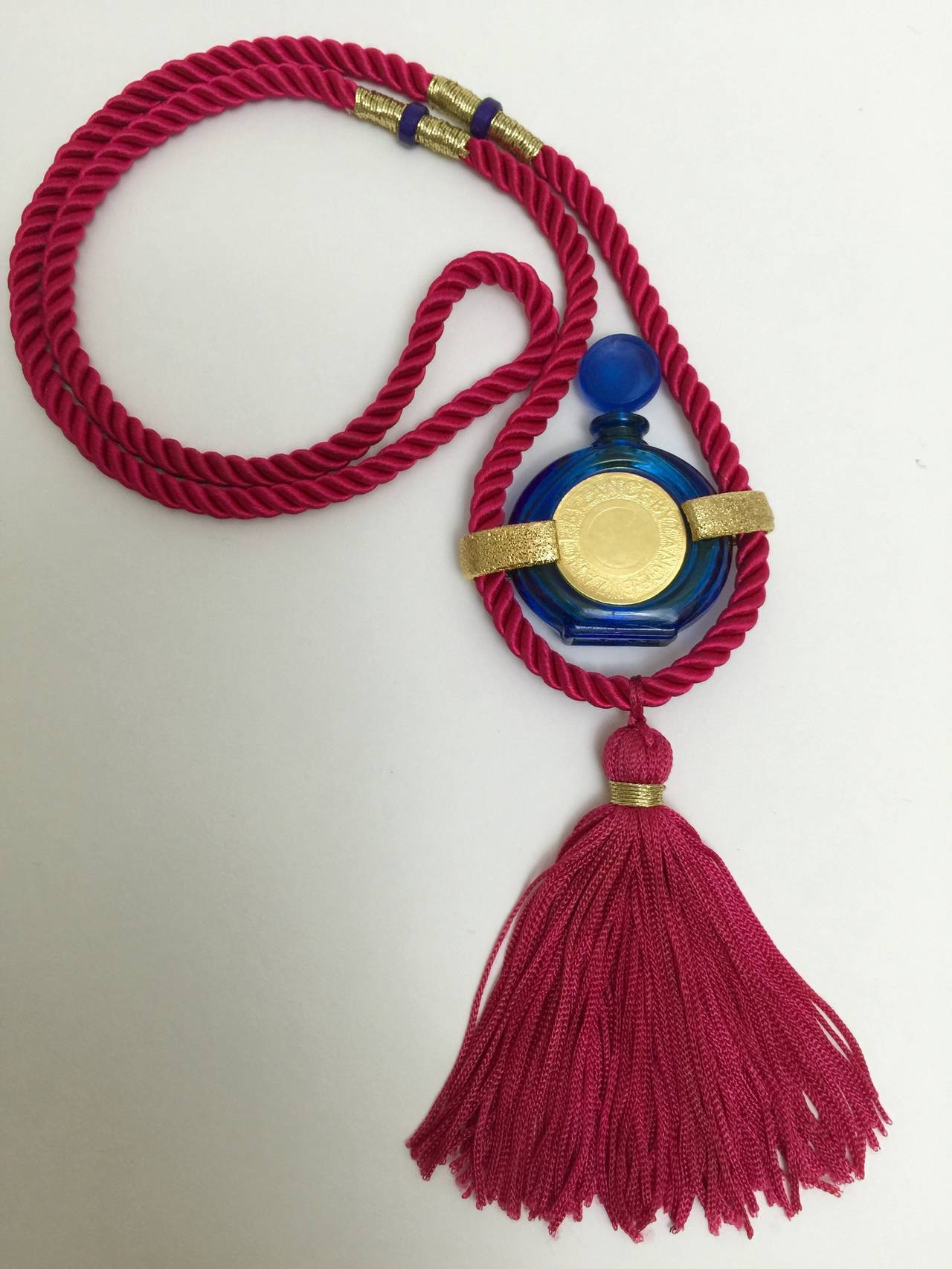Beautiful vintage Rochas  tassel perfume necklace.
I love the combination of the fuchsia pink silk cord, and the cobalt blue miniature perfume bottle. with all of the little gold metal details. 
The center of the bottle has textured round gold