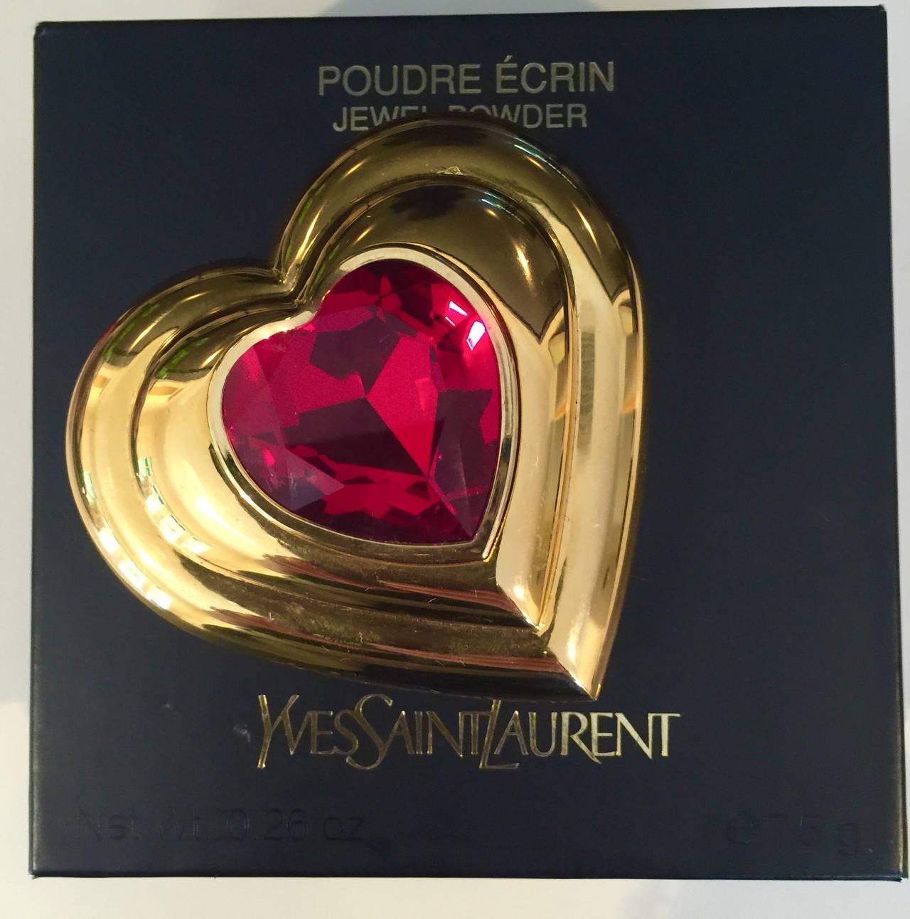 New Yves Saint Laurent Heart shaped Poudre Ecrin -Gold plated Jewel Powder Compact. Jewel  lid set with a Sparkly ruby red  stone. 
Interior Mirror. Made in France. Brand new in original box, never used. Beautiful, Collectable.

Measurements:
2.75