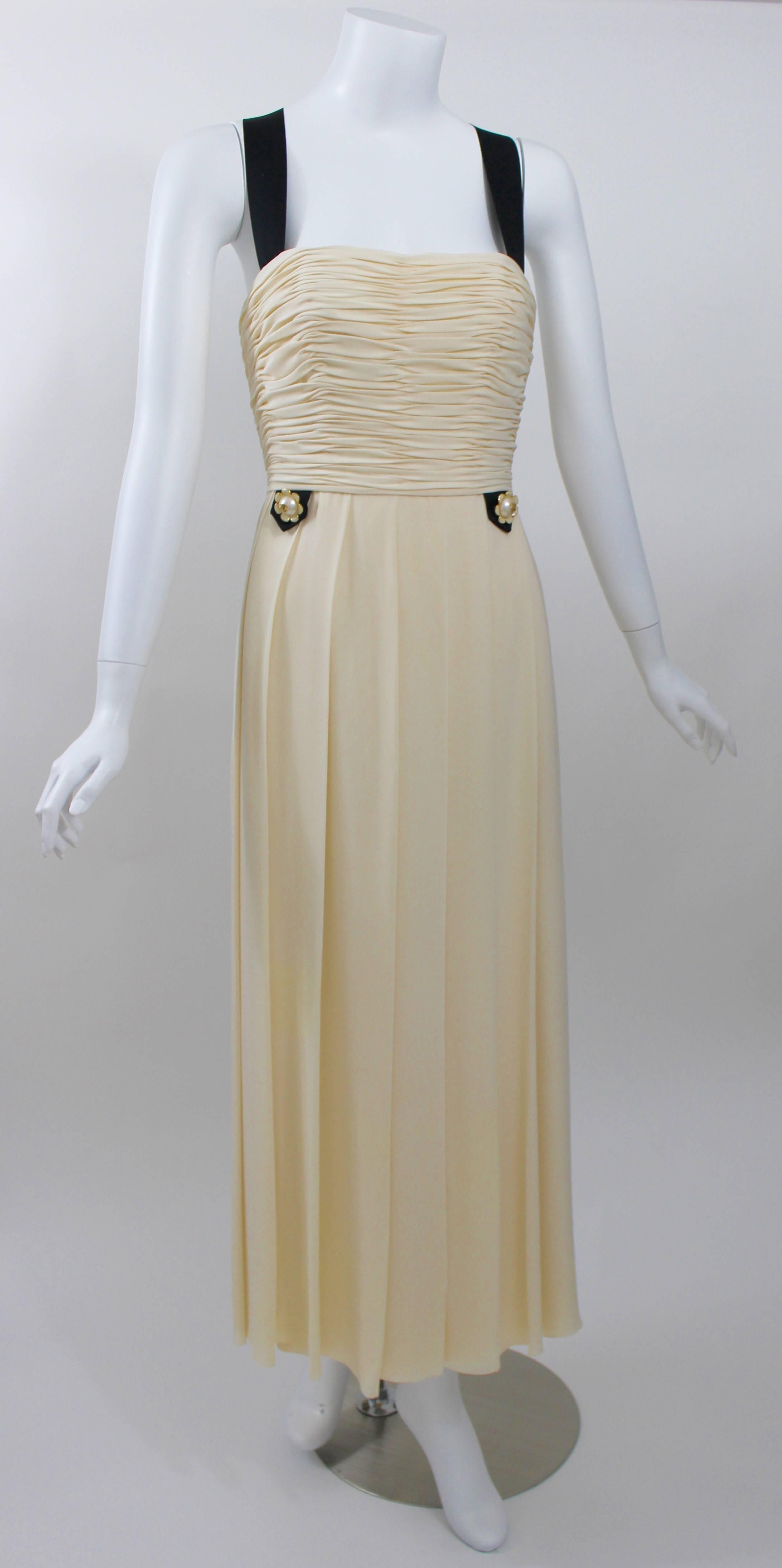 A gorgeous vintage Chanel dress in ivory silk chiffon with a gathered and boned bodice. 
Pleated skirt.
Black silk satin ribbon straps from the front of the dress that form a Y shape in the back. 
Six pearl buttons with the gold CC logo down the