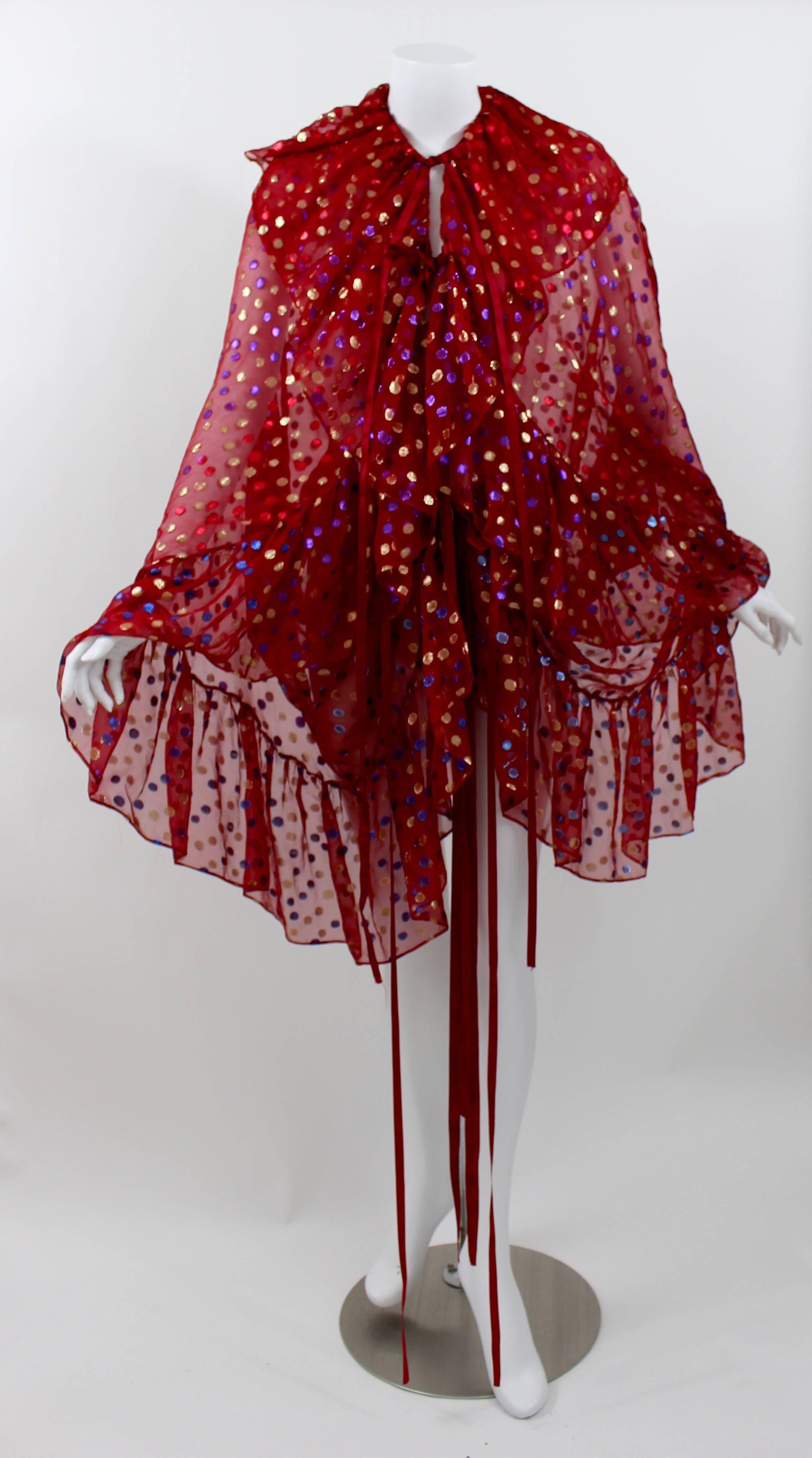 This is  a stunning vintage Saint Laurent  blouse in a glistening sheer red silk chiffon, with metallic golden, blue and purple  dots. 
Featuring a ruffle collar and cuffs.
Long red silk satin ribbons along the center of the top to tie and