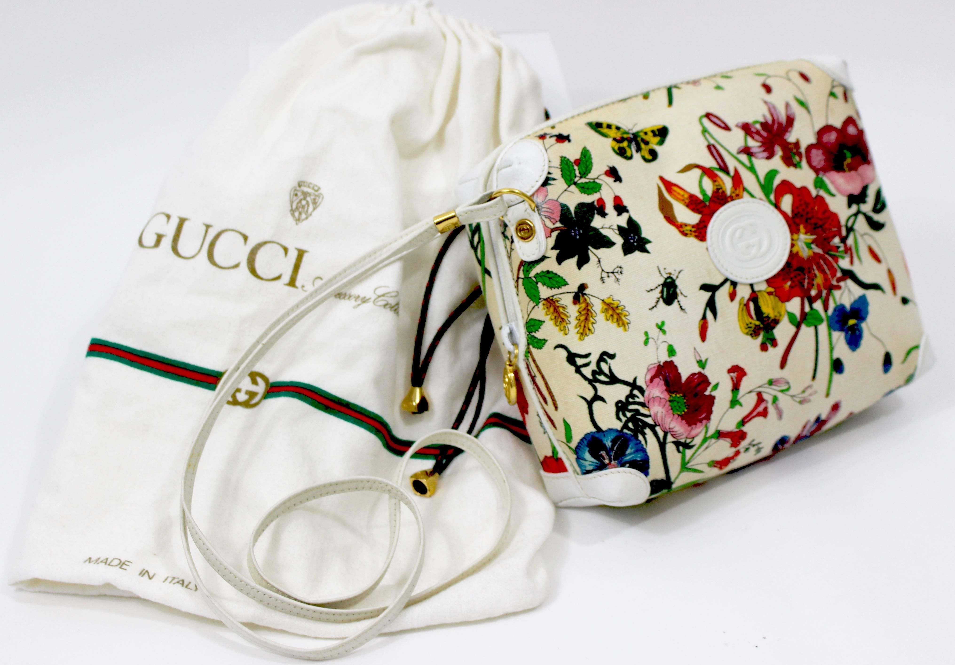 A 1970s Gucci white with colorful  floral and insect print canvas purse with  white leather trim on the corners, top of the bag  and  the long strap. The front of the bag has the GG signature embossed on the white leather. The gold hardware  on the