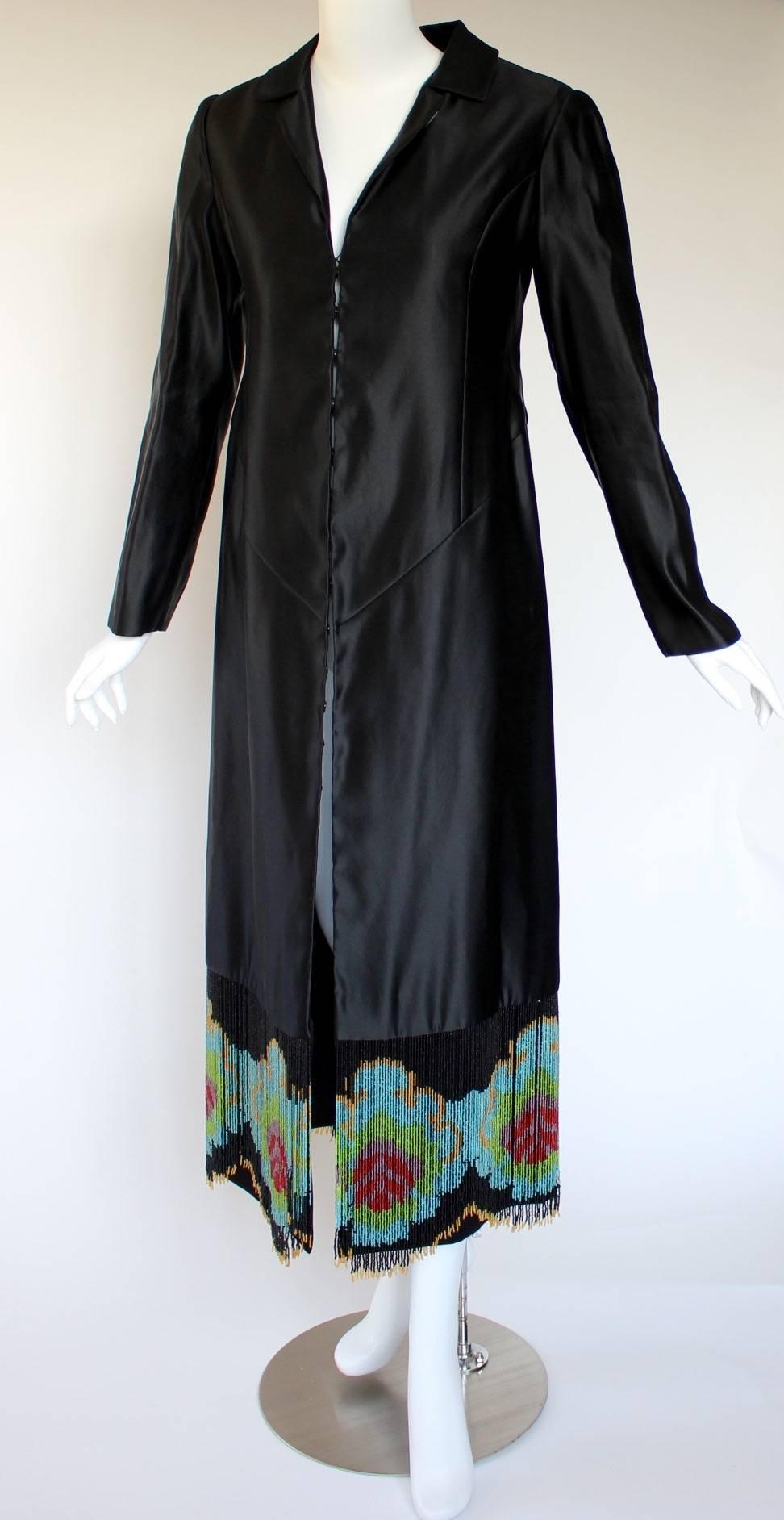 This is a one-of-a-kind piece, custom-made to perfection. Its origins began in Thailand, where the luxurious black silk was tailored into an Art Deco-inspired evening coat, with a notched collar, plunging neckline, seamed bodice, long sleeves and a