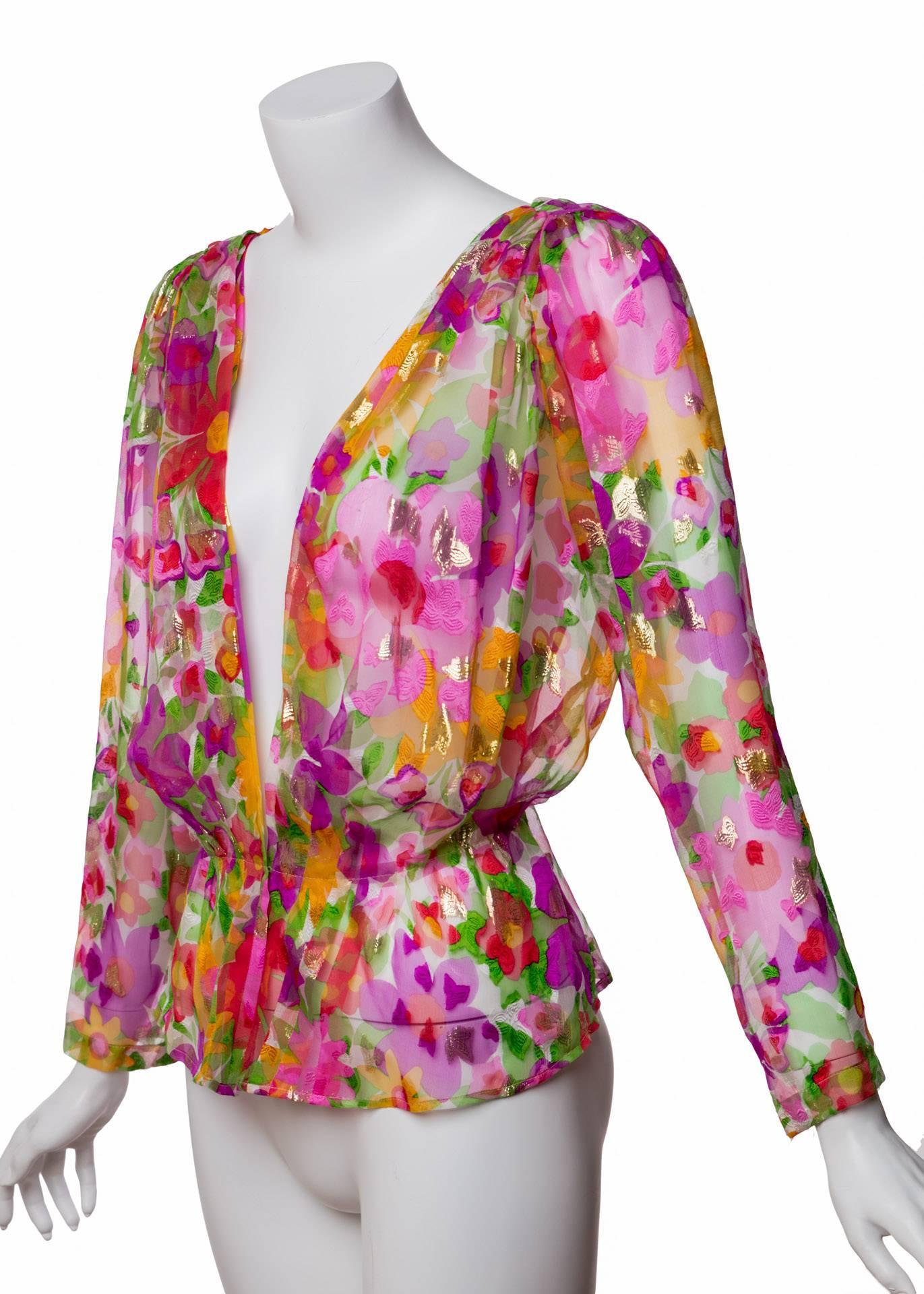 A stunning floral print flecked with gold and fuchsia throughout makes this Yves Saint Laurent blouse an incredible vintage find. Small and large blooms splash over a bed of white in a mouthwatering riot of poppy, violet, yellow and green, while