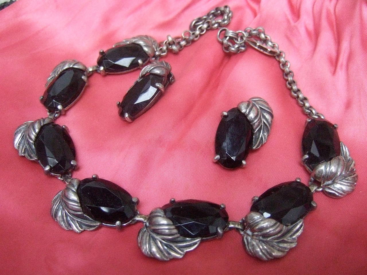            ****RESERVED SALE PENDING FOR ALLISON****

Schiaparelli Jet glass silver metal leaf necklace & earrings c 1950
The stylized necklace & earrings are designed with oval shaped faceted black glass settings accented with pewter tone metal