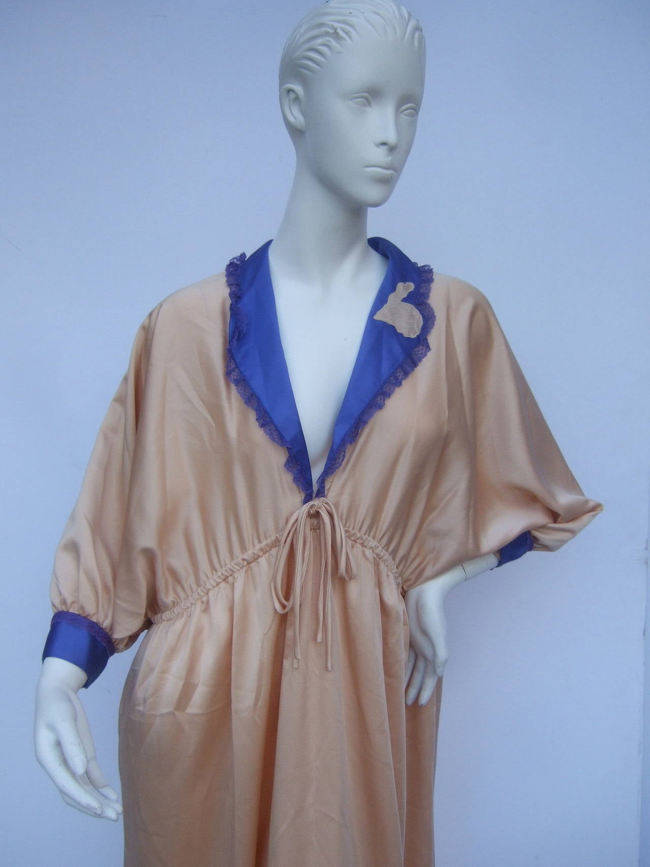 Zandra Rhodes luxurious peach lounge gown c 1980s 
The stylish gown is designed with Zandra Rhodes' signature empire drawstring silhouette. The elegant gown is designed with soft peach color polyester with a peacock blue lace trim collar &