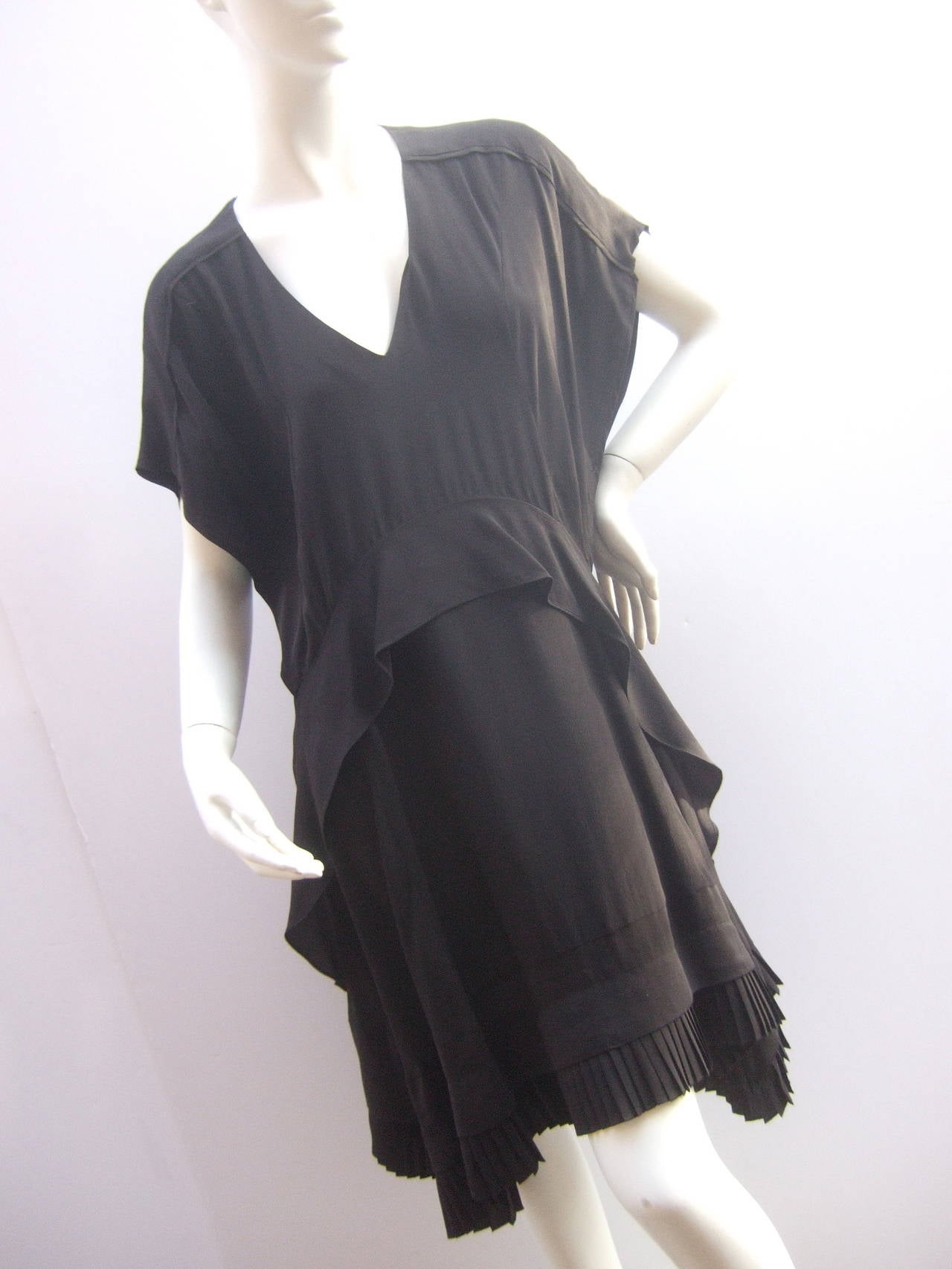 Balenciaga Sumptuous black silk dress. The elegant dress is designed with a bias peplum seam at the waist line that cascades down the front sides
The asymmetrical hemline is designed with accordion pleating that circles the hem. The pleated trim