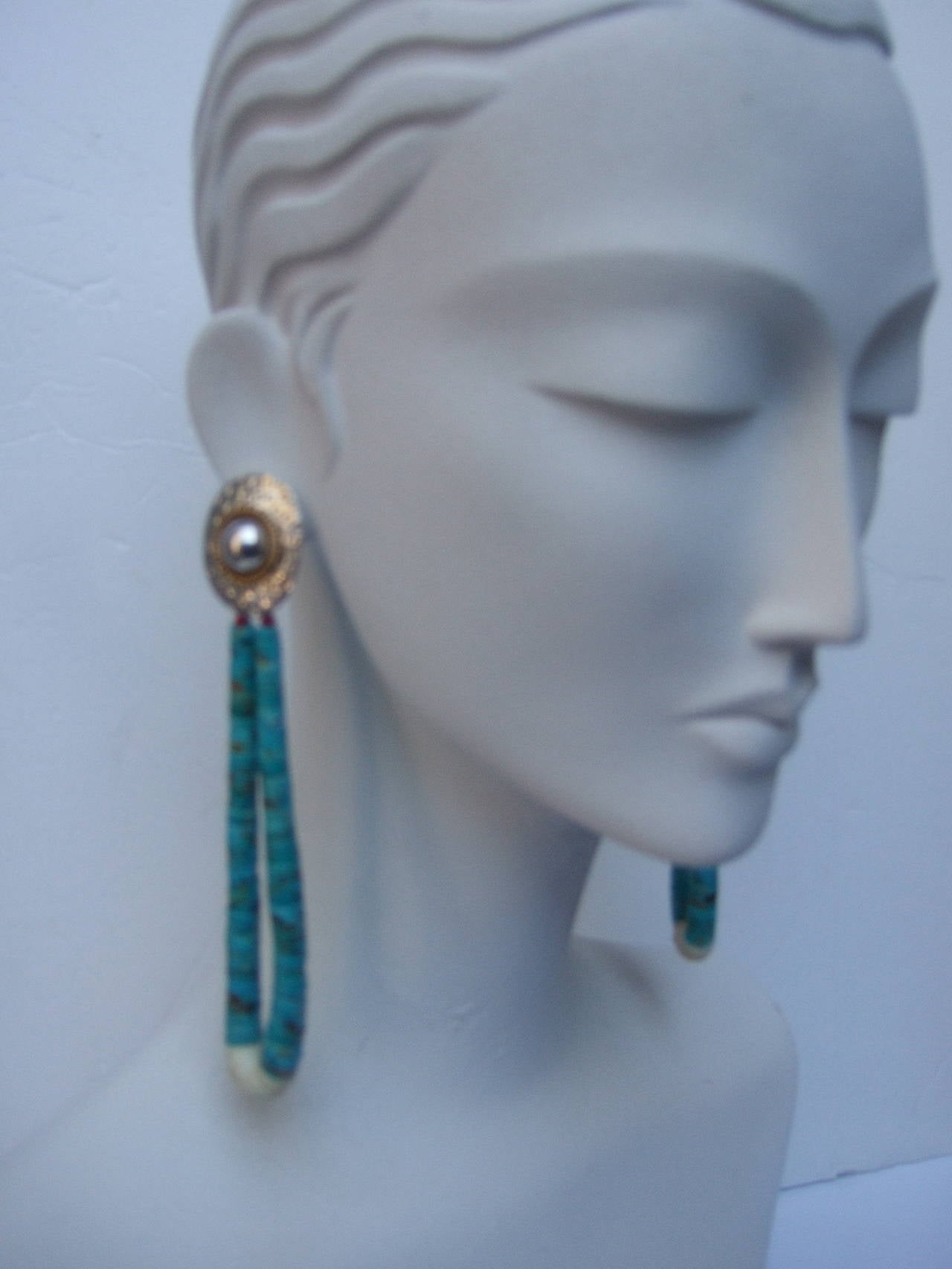 Artisan turquoise & sterling heisha pierced dangle earrings c 1970s
The massive handmade earrings are designed with hand rolled graduated turquoise sliced stones. The tribal style pierced earrings hang from a hammered sterling oval disc that has a