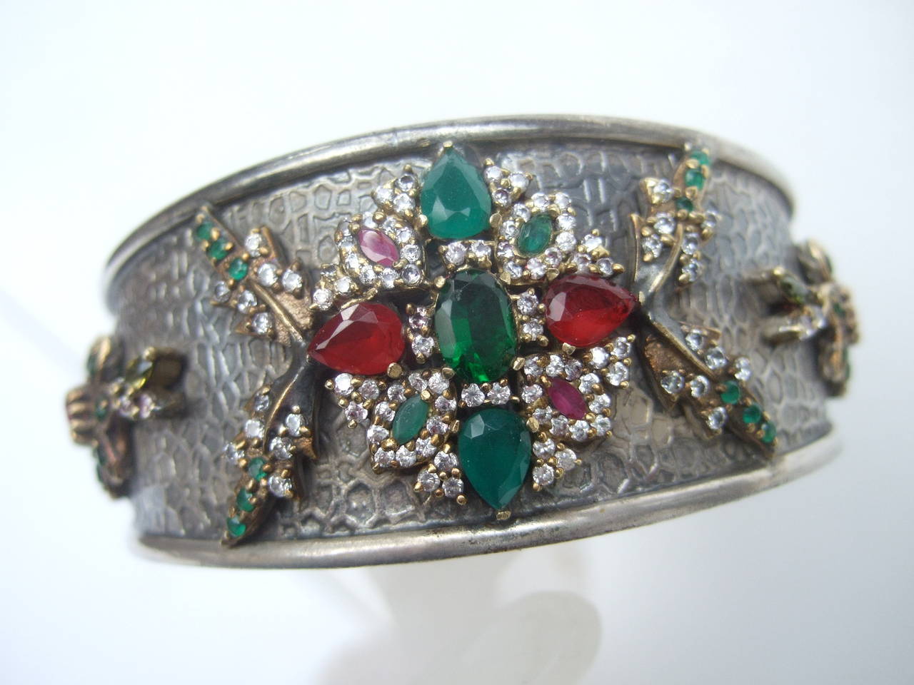 Opulent jewel encrusted sterling silver cuff bracelet. The elegant cuff is embellished with emerald green & ruby color crystals. The jewel tone crystals are embellished with glittering diamante settings

The sterling cuff is accented with a
