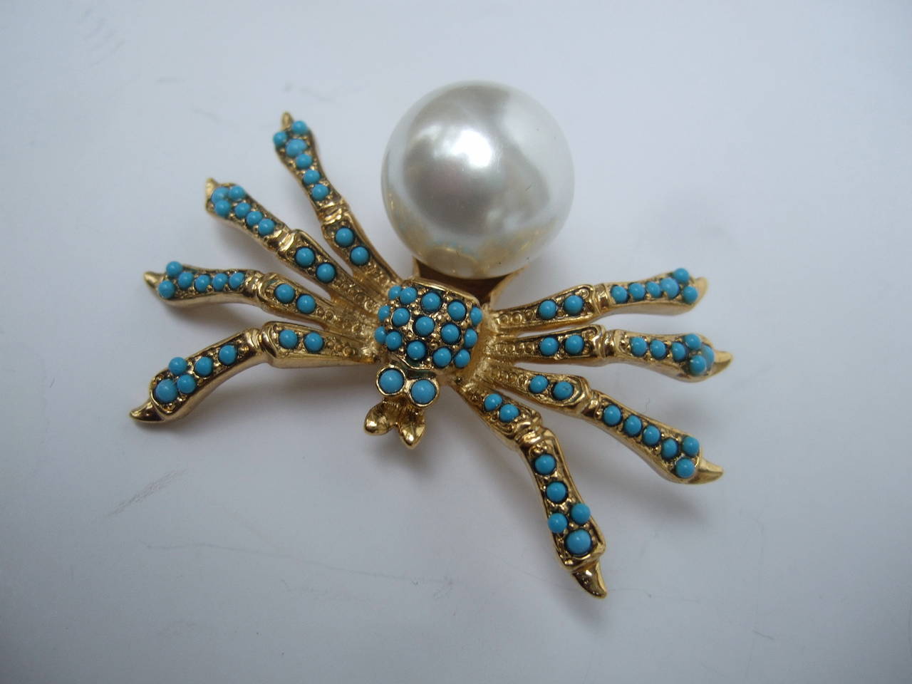 Kenneth Lane Jeweled spider brooch. The unique brooch is embellished with a lustrous enamel resin pearl accented with tiny turquoise color resin beads
The figural spider brooch is designed with gilt metal & stamped: Kenneth Lane

The avant-garde