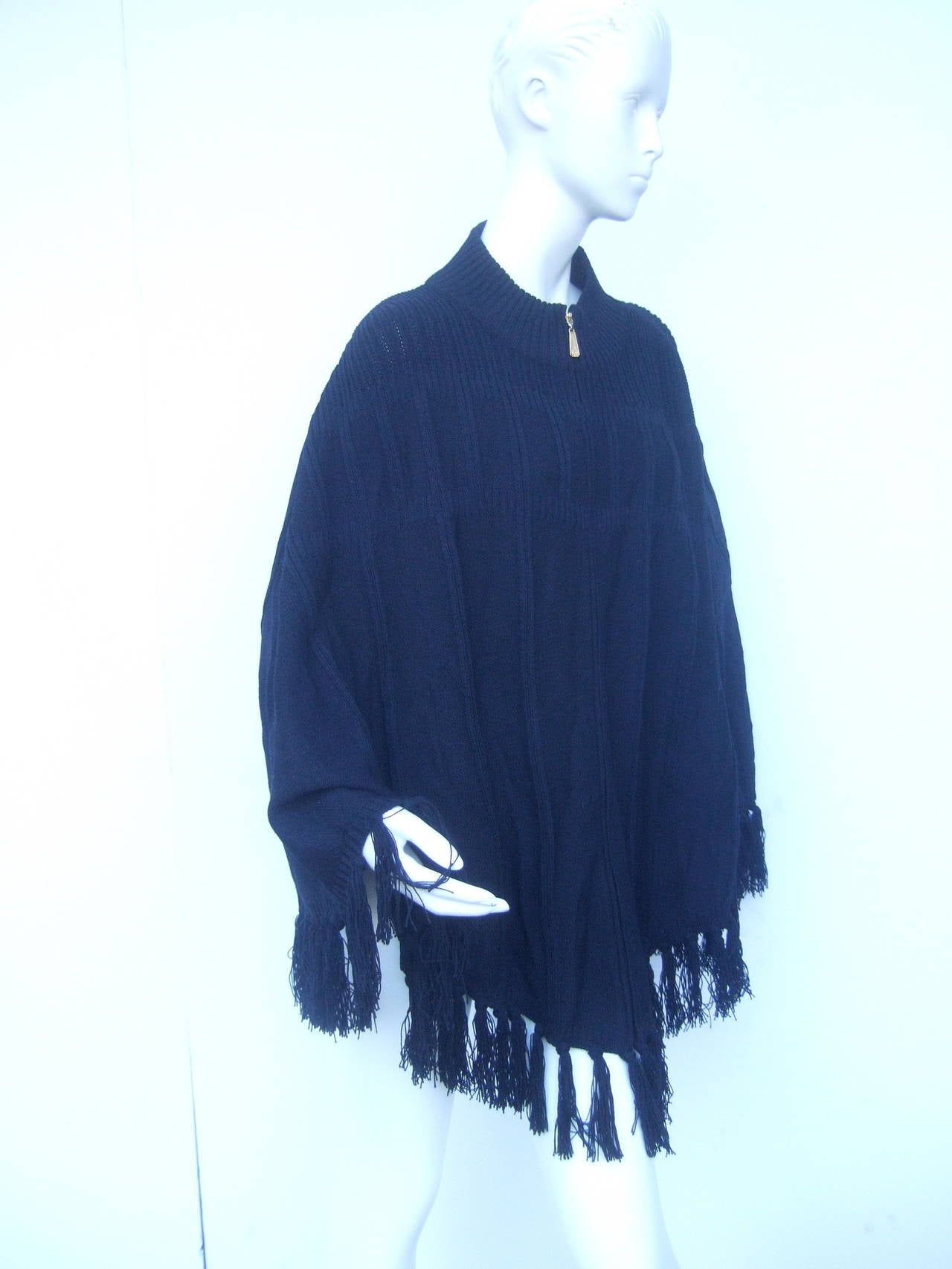 St John Sport Black fringe knit zippered poncho c 1990s
The stylish wool knit poncho is designed with ribbed detail on the neckline that frames the shoulders. The high fashion knit poncho zippers up the front with a gilt metal zipper pull inscribed