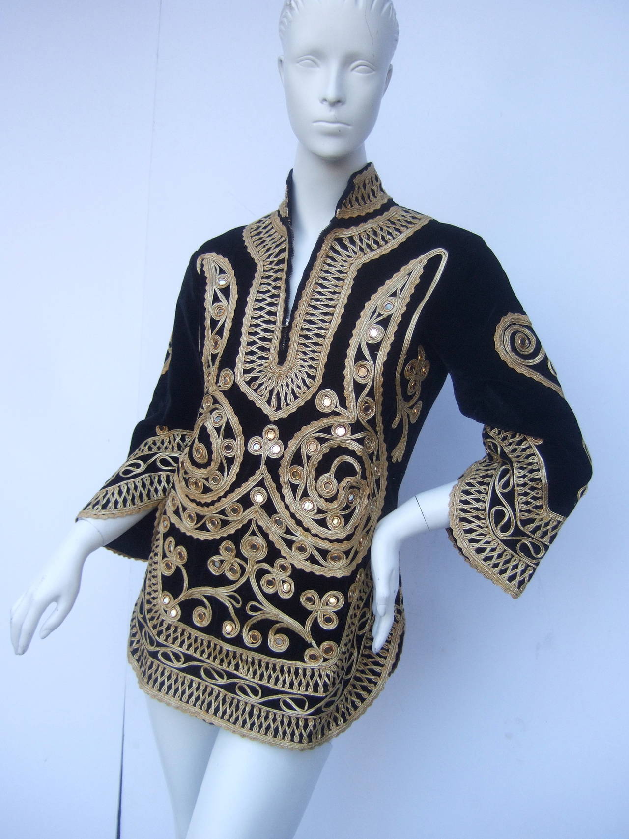 Exotic black velveteen gold metallic applique tunic c 1970s
The ethic velveteen tunic is embellished with elaborate gold metallic applique designs throughout. The zippered collar is framed with ornate applique that extends to the sleeves & runs