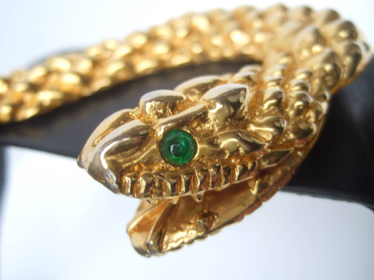 Judith Leiber Ornate gilt metal serpent black leather belt c 1980s
The avant-garde wide black leather belt is adorned with a massive gilt metal coiled serpent embellished with green glass cabochon eyes & textured gilt metal that emulates