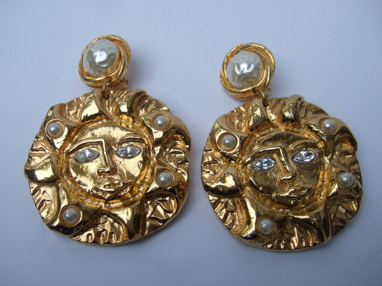 Massive gilt jeweled sun earrings designd by Dominique Paris c 1980s
The unique large scale runway style earrings are designed with a dangling sun medallions. The gilded sun is embellished with diamante crystal eyes with resin enamel pearls