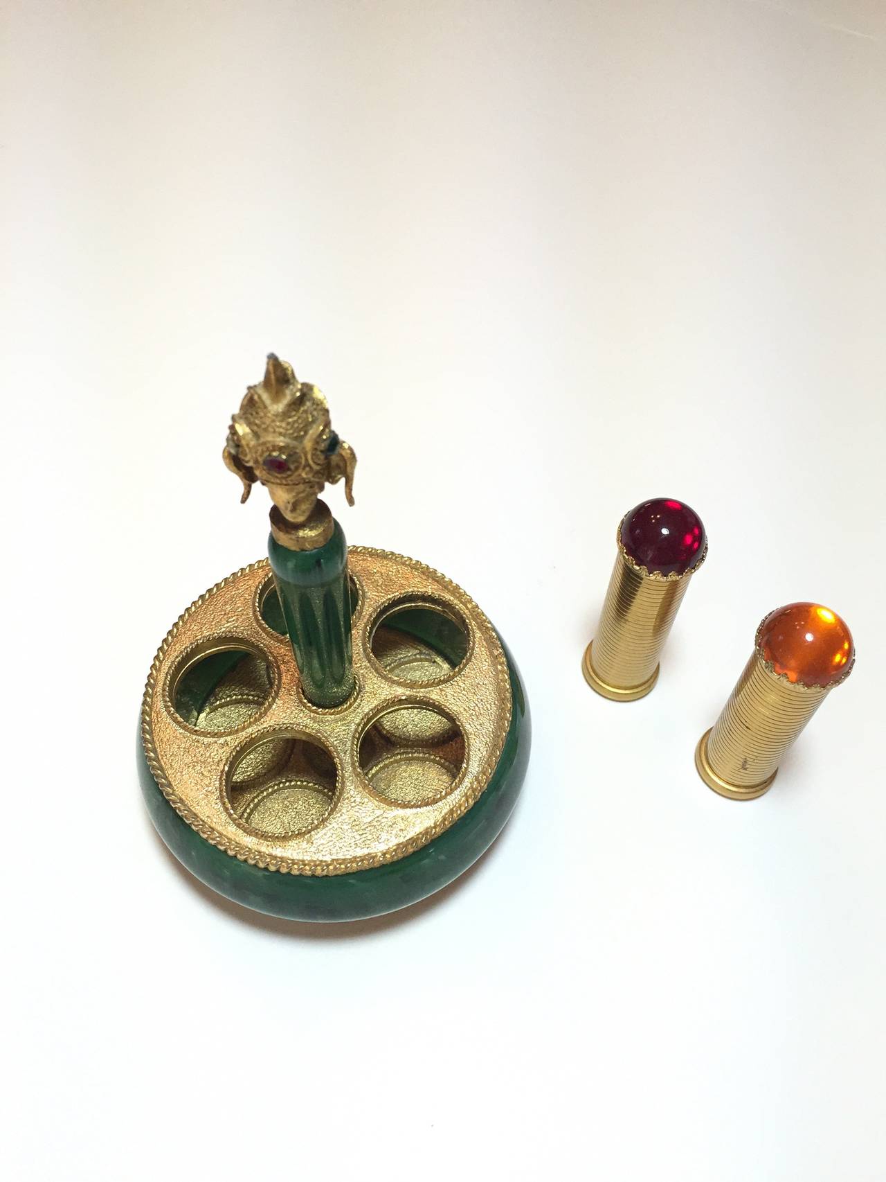 What a wonderful and unusual vanity item!  This lipstick holder, by beauty legend, Helena Rubenstein, features a Far East inspired base that displays 5 lipstick holders each topped with a paste cabochon.  We have two faux rubies, one faux emerald,