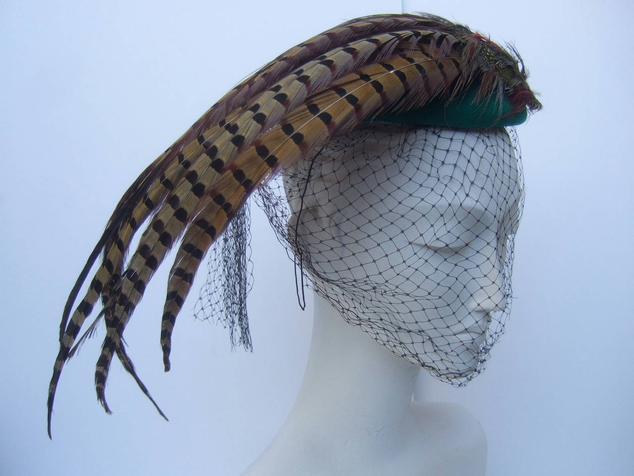 Dramatic green felt feather veiled hat c 1980s
The retro inspired stylish hat is embellished with long exotic feathers
The high fashion hat is designed with an emerald green felt wool dome 
accented with a black net veil

Designed by Liz