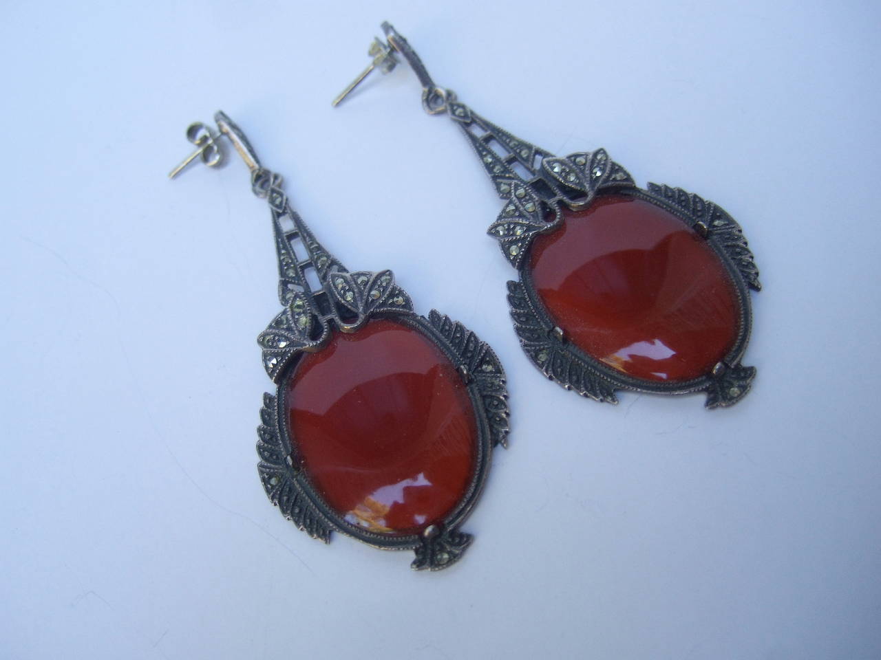 Exquisite dangling carnelian glass marcasite earrings c 1950s
The ornate art deco pendant style pierced earrings are designed
with large carnelian smooth oval shaped glass stones

The large opaque stones are encased is pewter tone