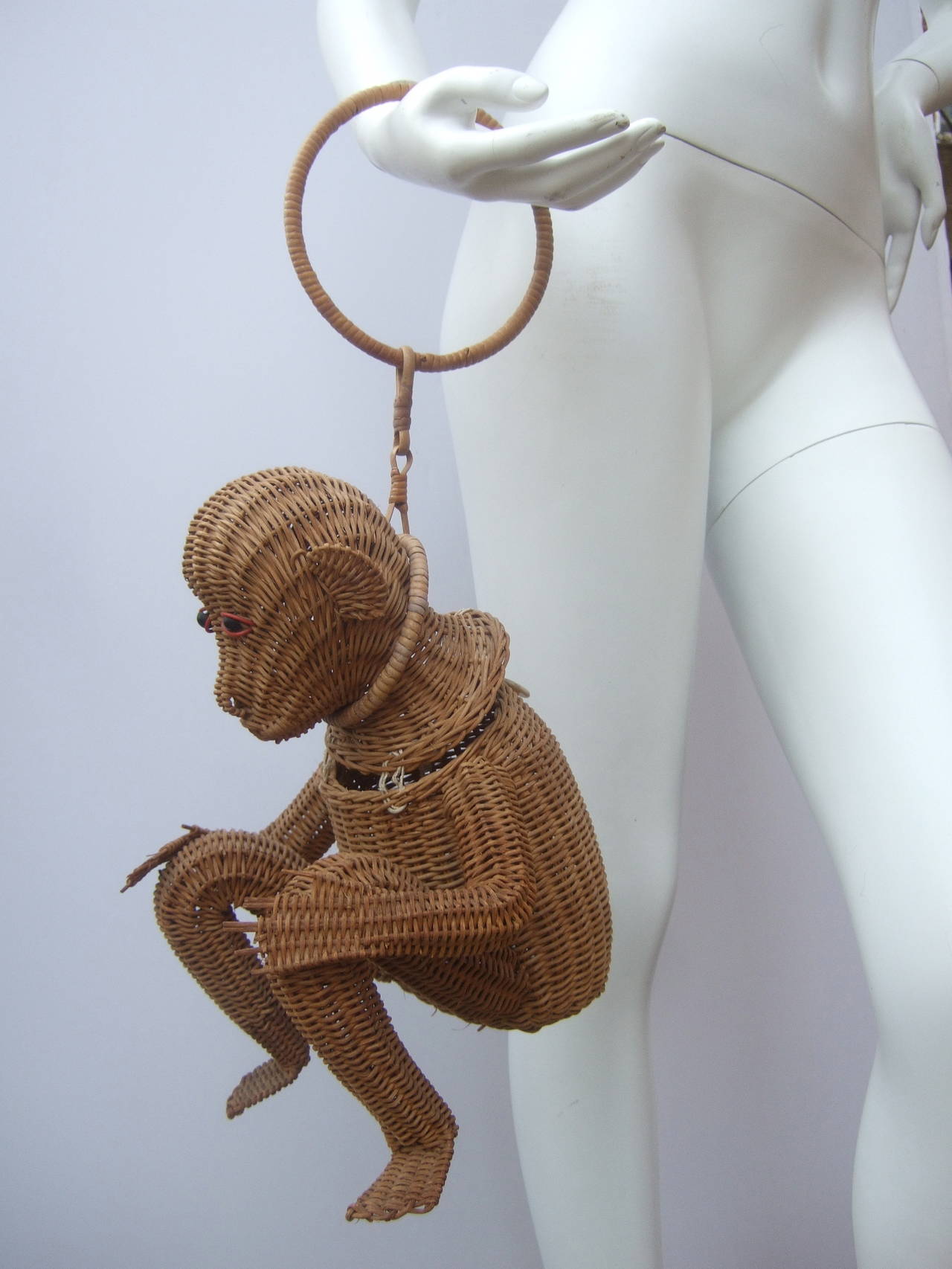 Whimsical wicker handmade monkey handbag c 1960
The unique retro handbag is designed in the shape of a monkey figure
The little guy is accented with black wood beaded expressive eyes
The avant-garde handbag hangs from an attached round hoop