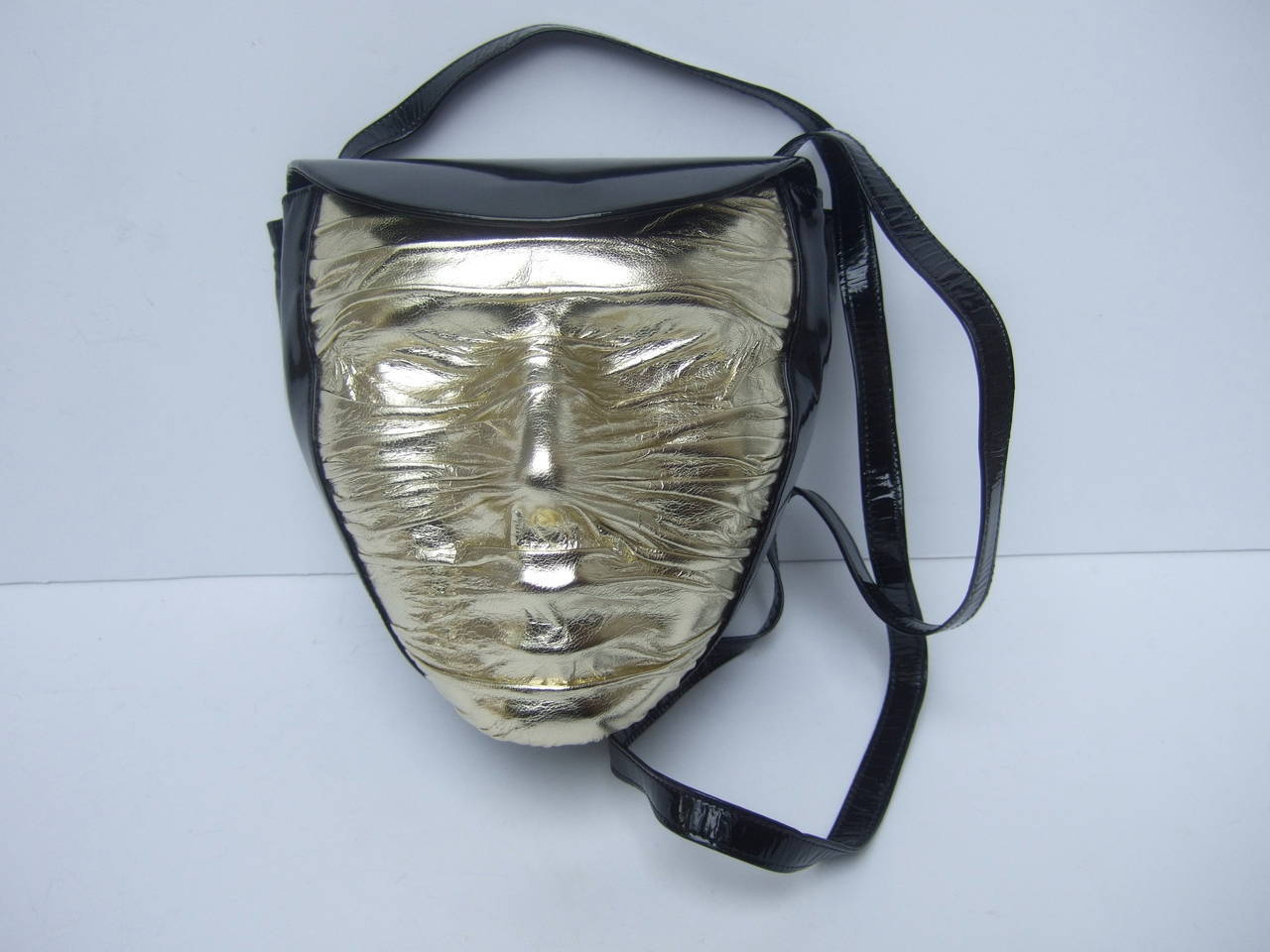 Charles Jourdan Paris Avant-garde mummy handbag c 1980s
The surrealistic high fashion shoulder bag is designed with 
a bizarre face that is covered with gold metallic stretched leather
The facial features are illuminated under the gold leather