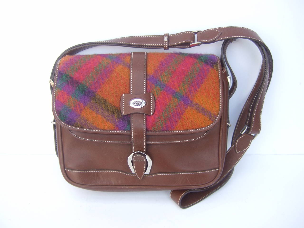 Gucci Italy Rare plaid wool brown leather shoulder bag c 1980s
The unique saddle style handbag is designed with a multicolor plaid wool flap cover. The center of the front cover has a silver metal designer plate
with Gucci's interlocked