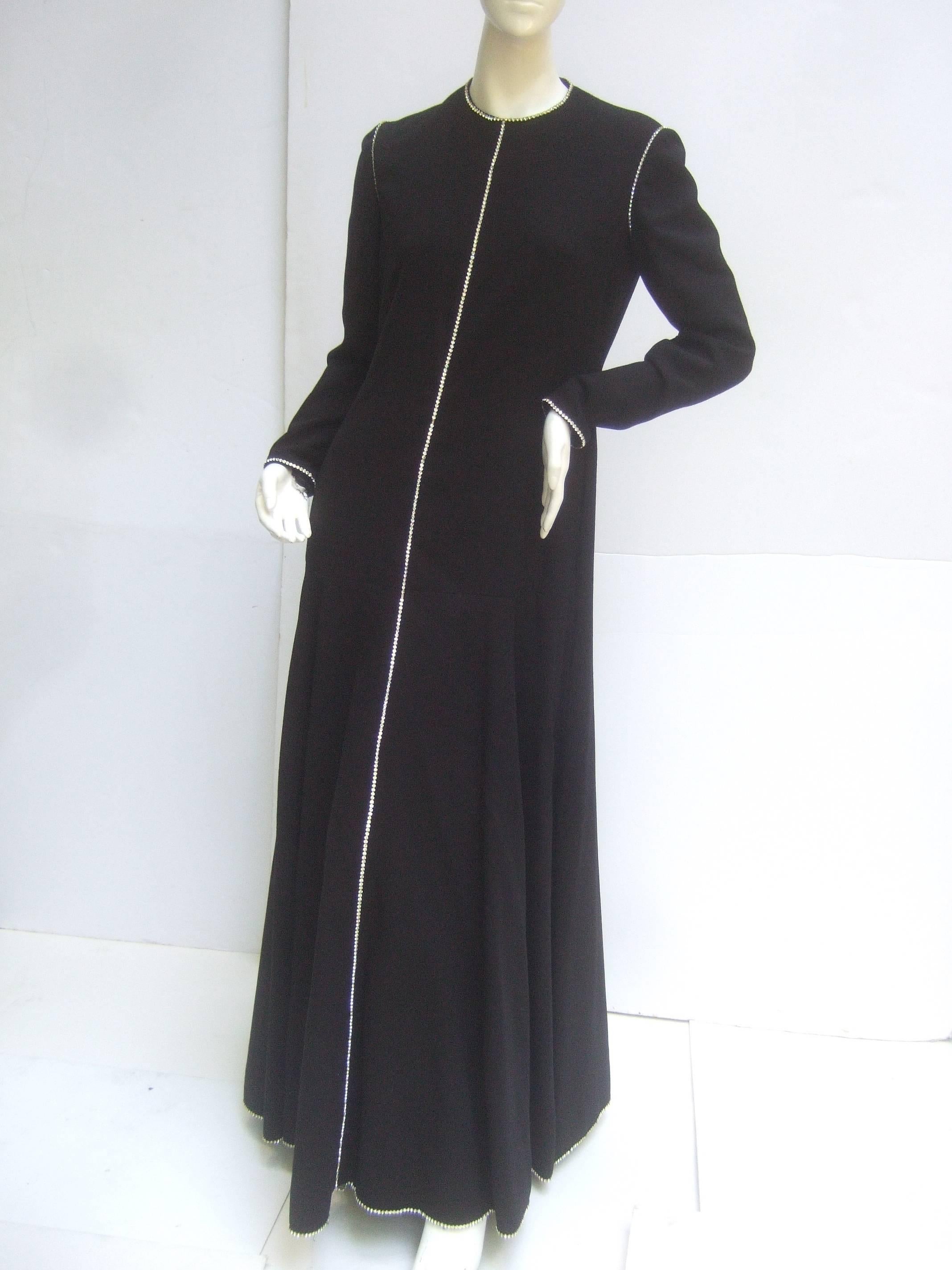 Geoffrey Beene Stunning black wool crystal trim gown c 1970
The elegant sweeping black wool gown is embellished
with a diamante crystal border that circles the neckline, 
runs down the center, frames the sleeve cuffs, extends 
to the shoulders