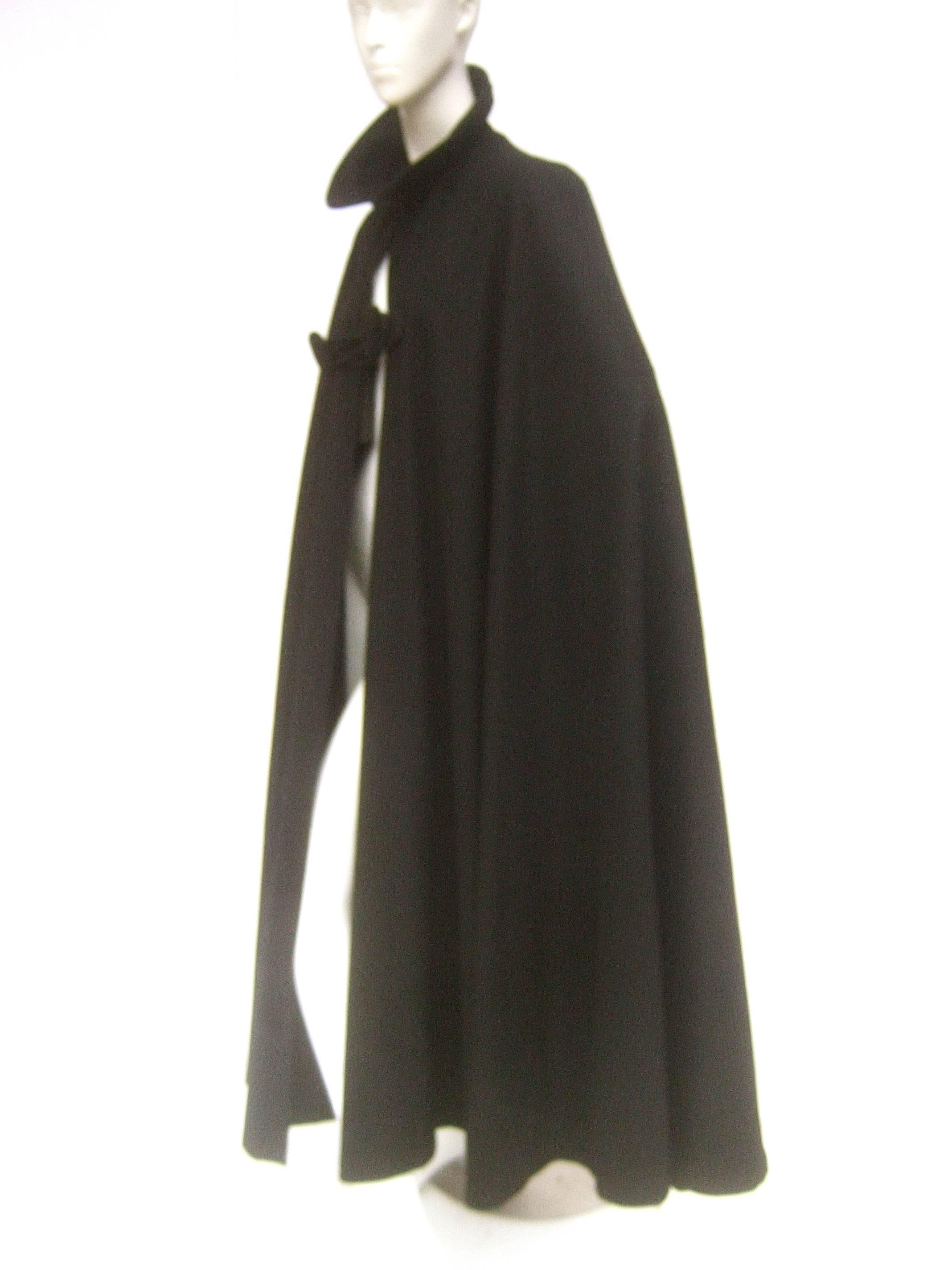 Dramatic long sweeping wool cape by C.C. Almy Fifth Ave
The elegant long wool cape is designed with 
a single large rope knotted frog style closure

When secured the voluminous draped silhouette
partially reveals the garments worn underneath